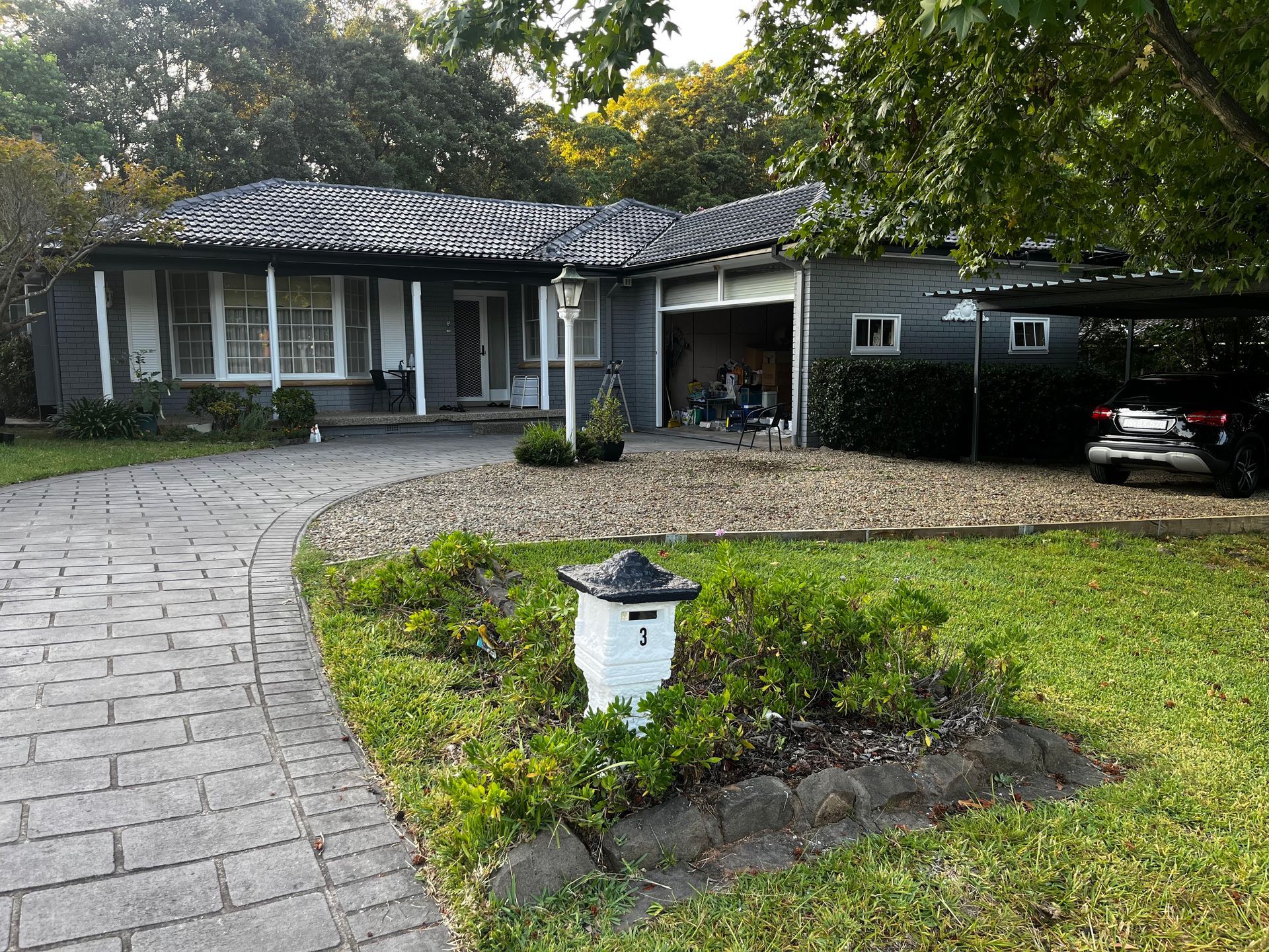 A low-angle view of a white, single-story house with a grey corrugated metal roof under a bright, sunny sky.