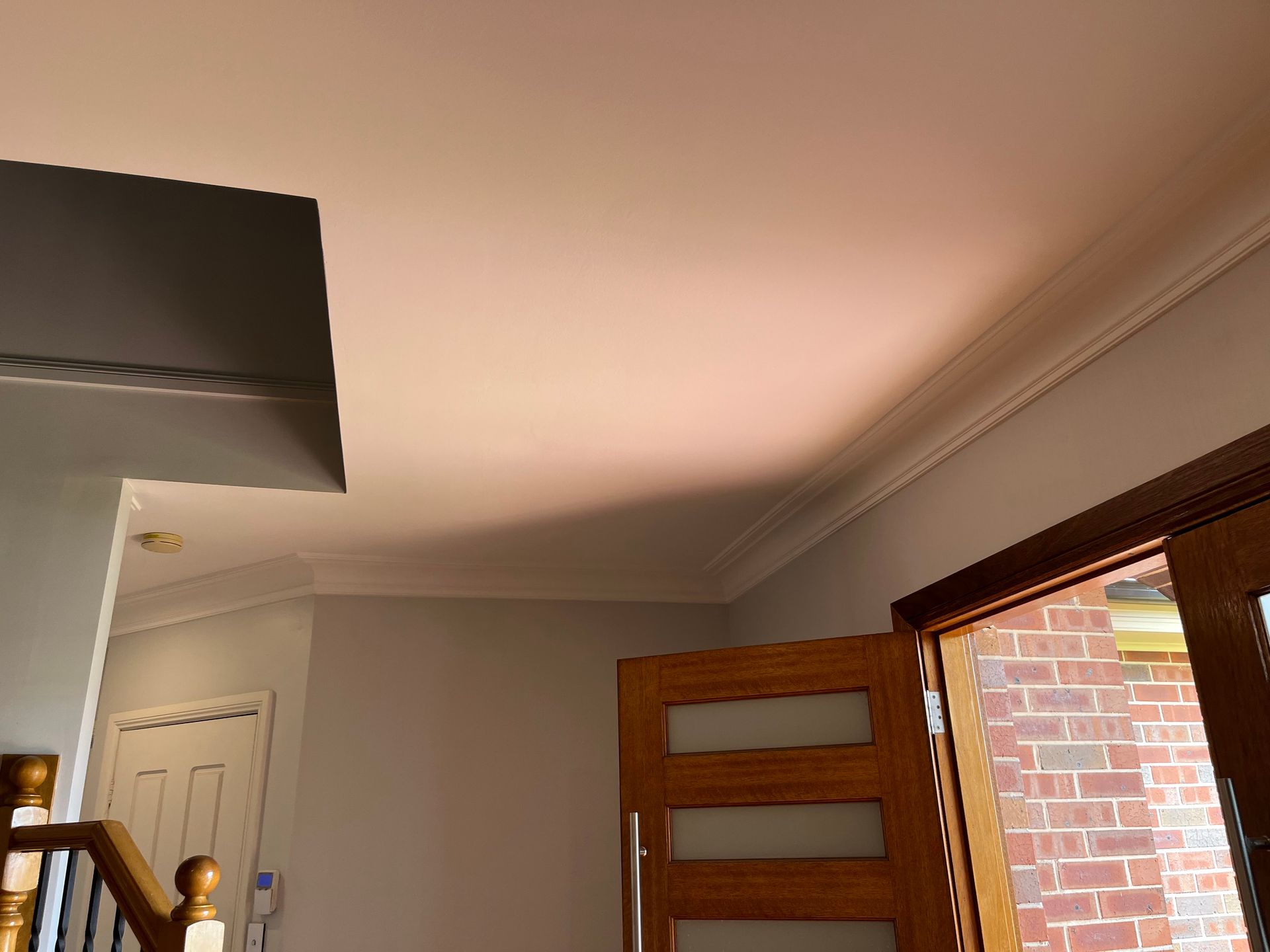 An interior view showing a white ceiling with crown molding, a dark wooden door with frosted panels, and brick exterior.