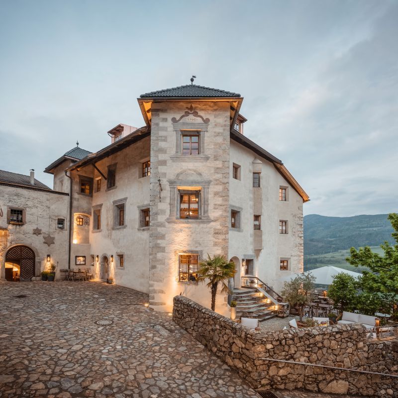 Castle with stone facade, courtyard, and tower illuminated at dusk.