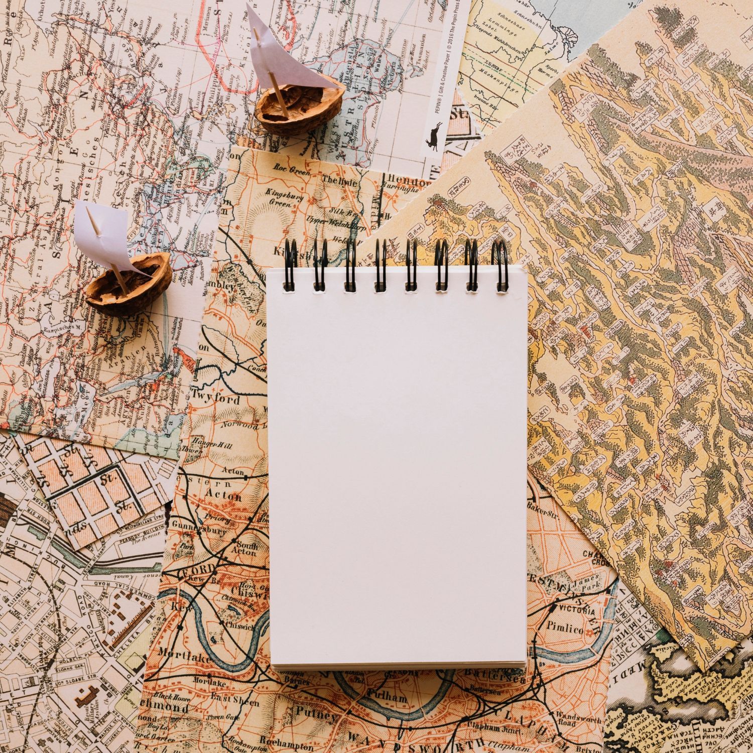 Notepad on map, with nut shells and paper boat.
