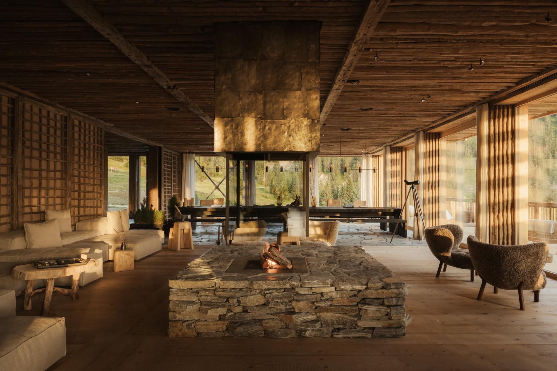 Cozy wooden lodge interior with a stone fireplace, billiards table, and large windows with outdoor views.