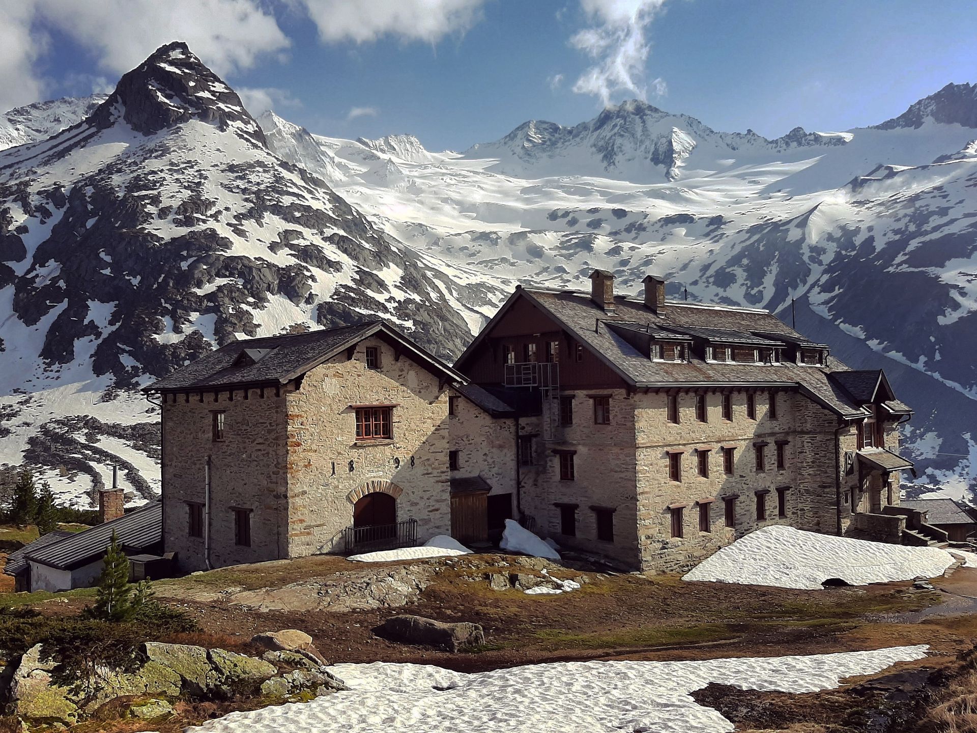 Stone buildings nestled against snow-capped mountains. Small patches of snow on the ground.