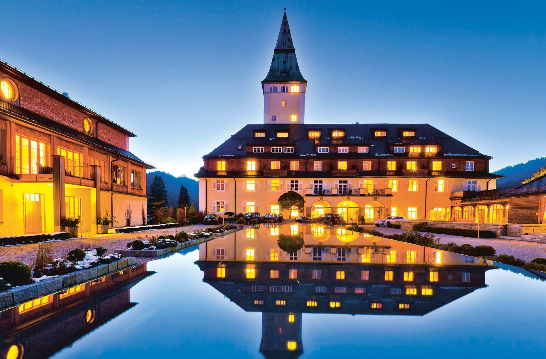 Hotel illuminated at dusk, reflecting in still water, with a tall tower.