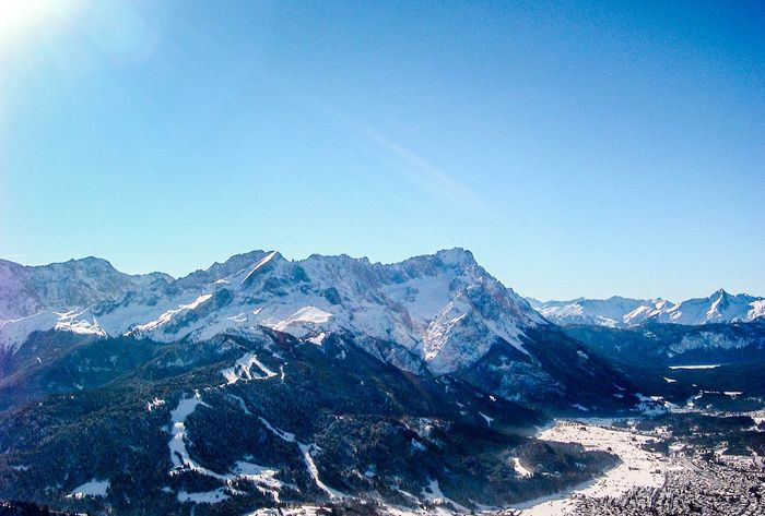 Snowy mountain village at dusk, lights glow, surrounded by peaks and a colorful sky.