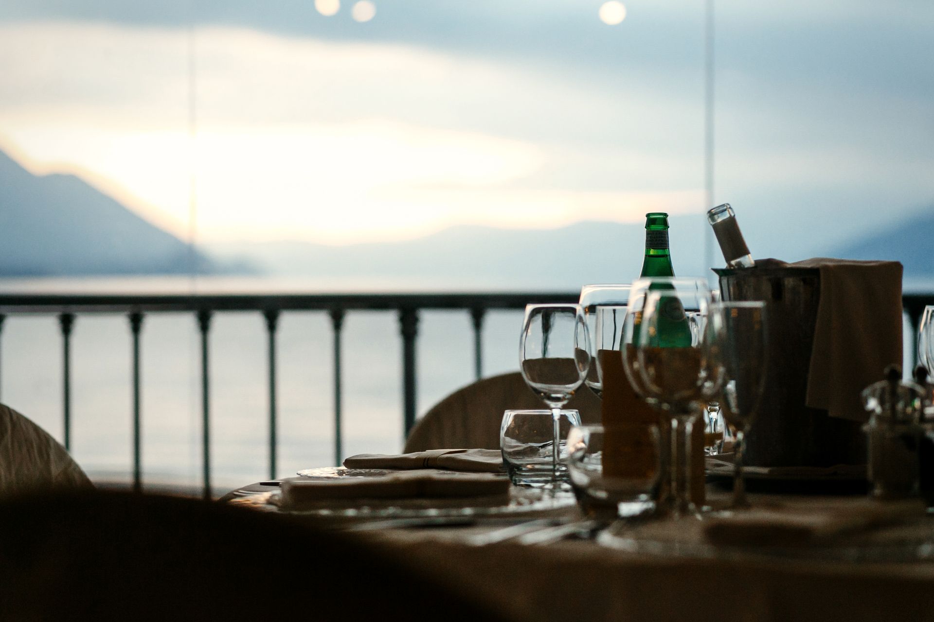 Table set for a meal, overlooking a lake and mountains. Includes wine glasses, bottles, and a wooden ice bucket.