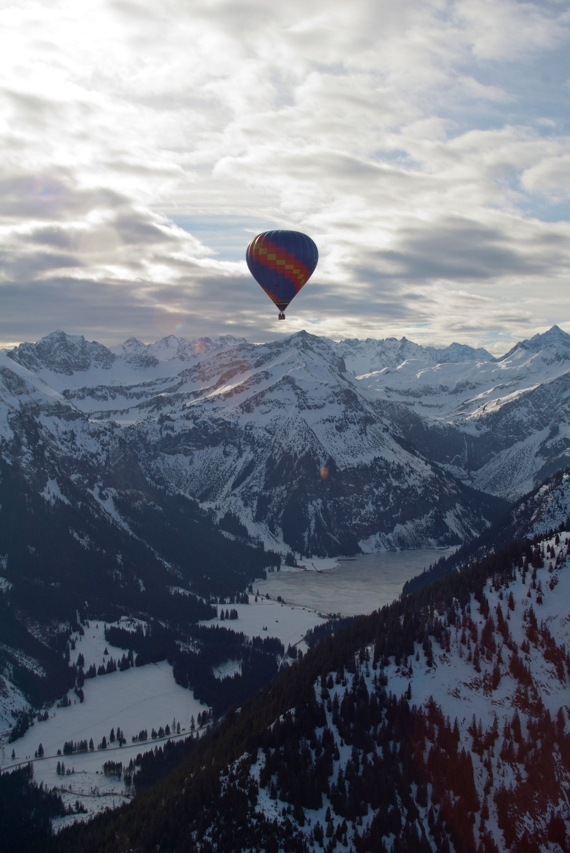 Hot air balloon over snow-covered mountains, sunlit sky above.