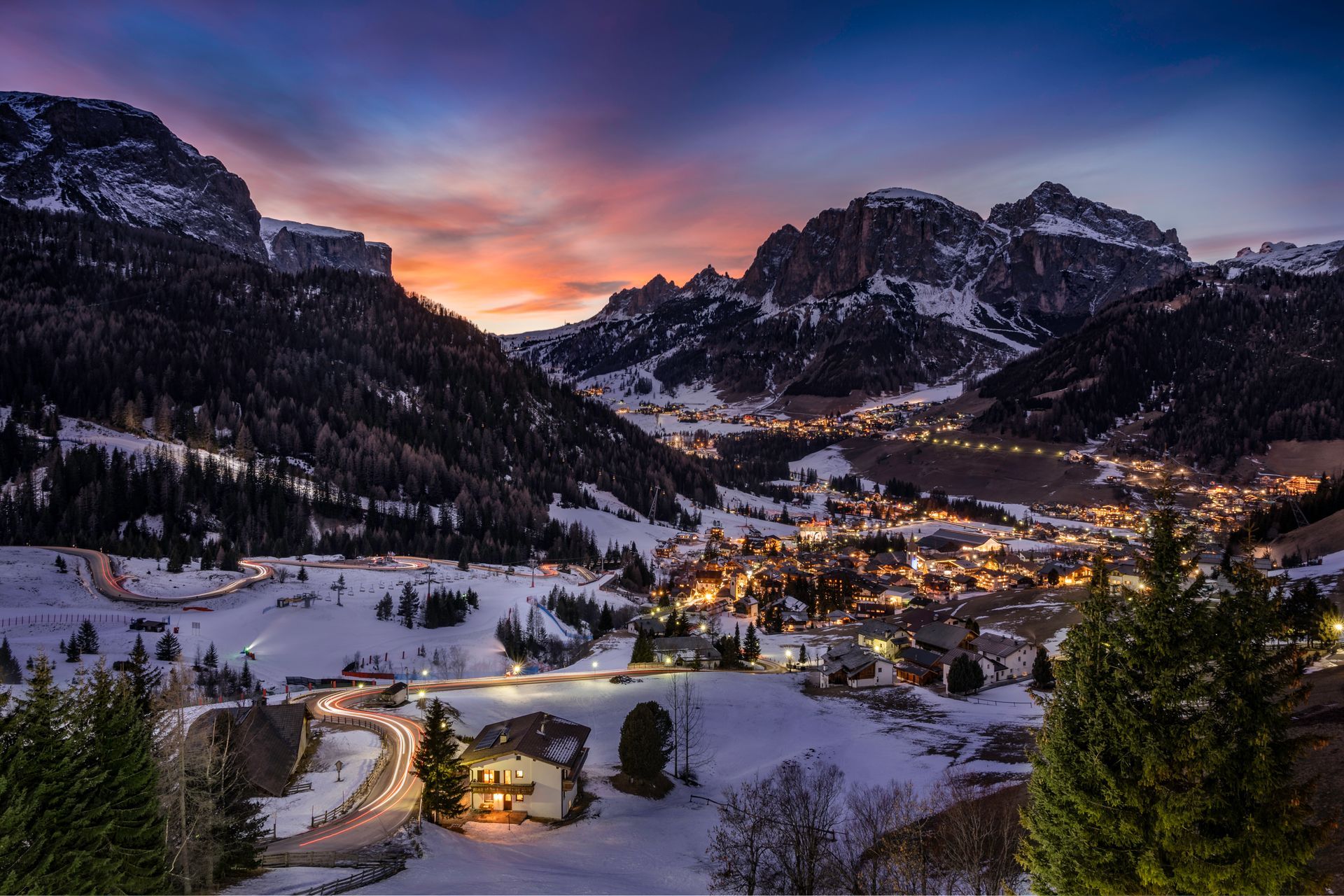 Snowy mountain village at dusk, lights twinkling, with colorful sky.