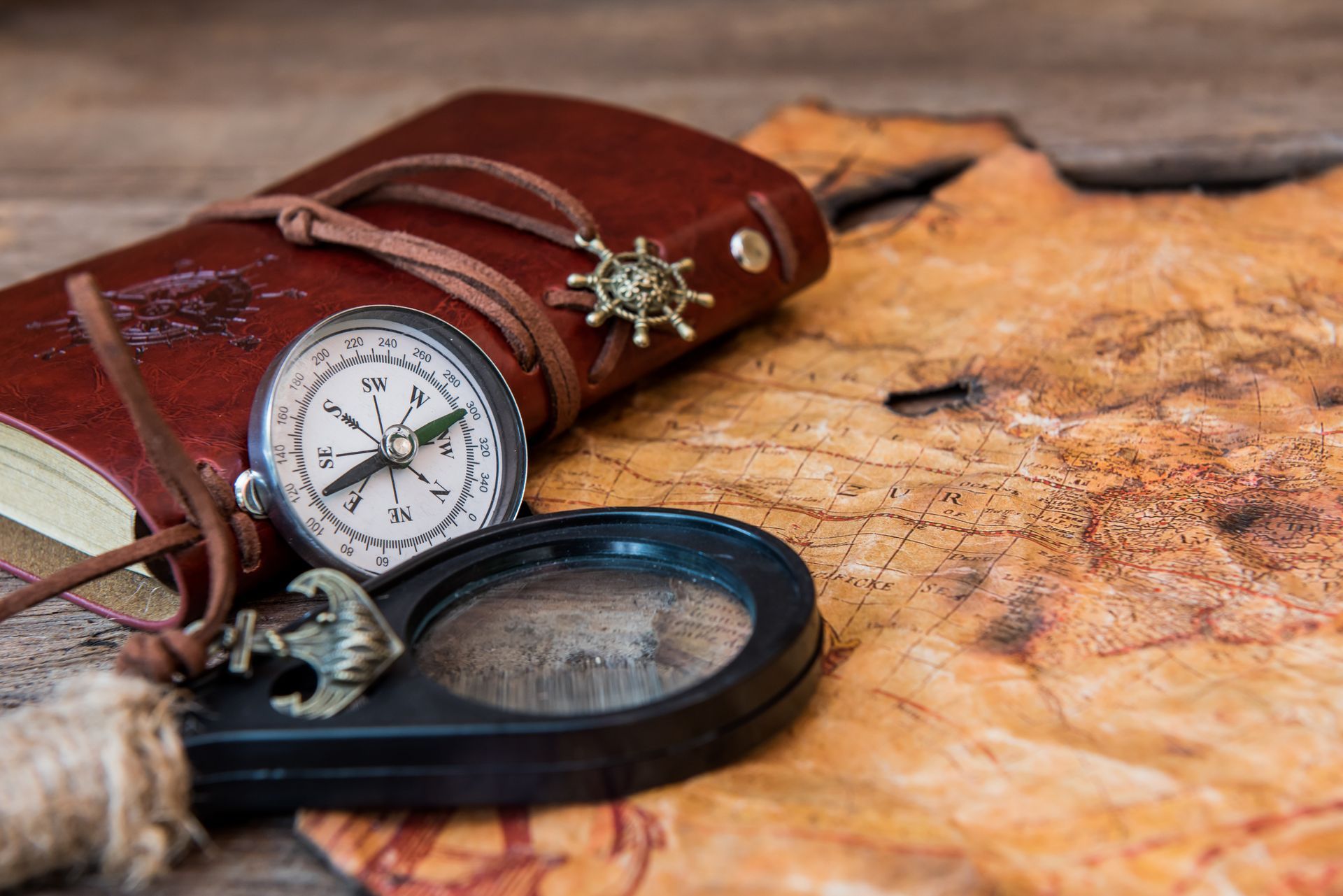 Compass, magnifying glass, and journal on a map, evoking travel and exploration.