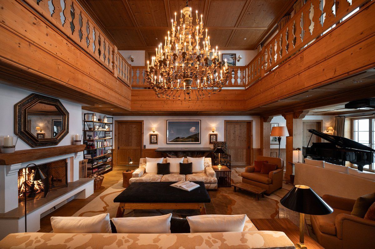 Luxurious chalet living room with grand chandelier, fireplace, and balcony.