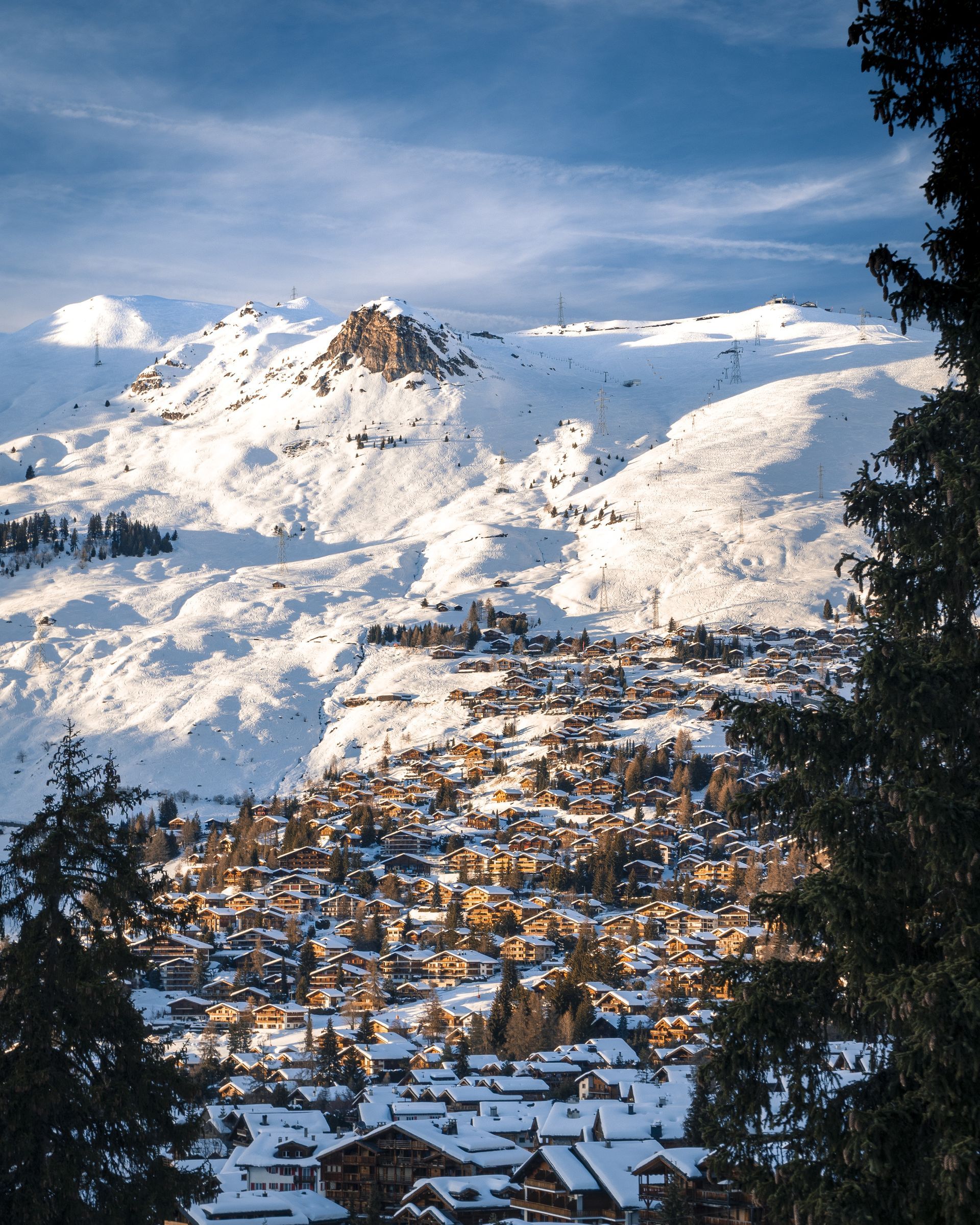 Snowy mountain town nestled in a valley, bathed in sunlight. Peaks and trees frame the scene.