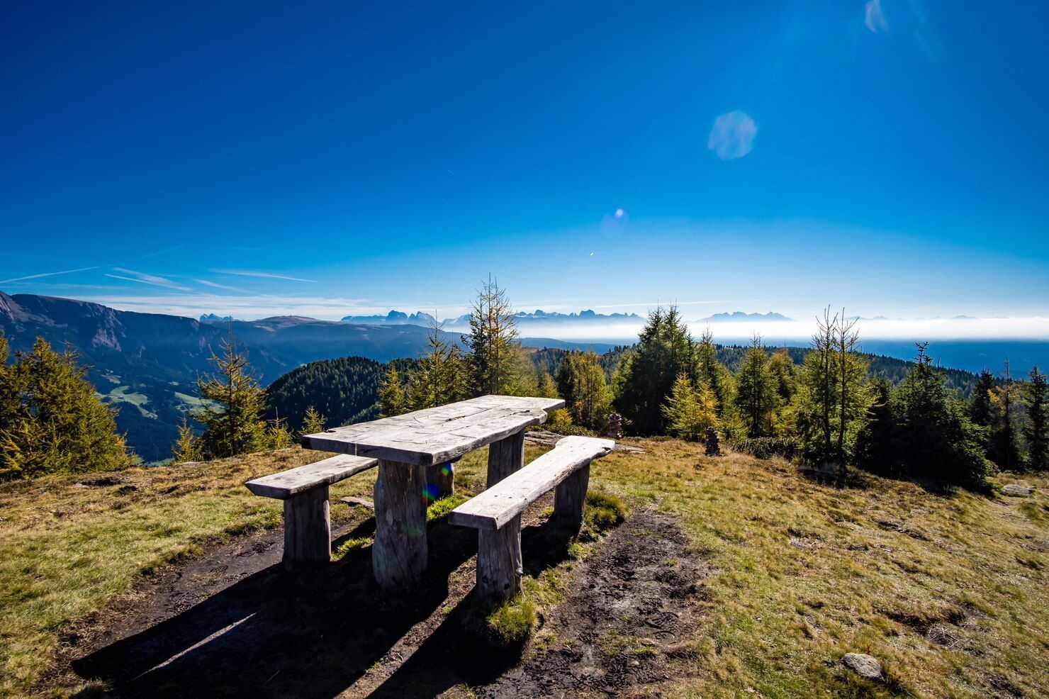 Picnic table on a mountain peak with a scenic view of a landscape under a clear blue sky.