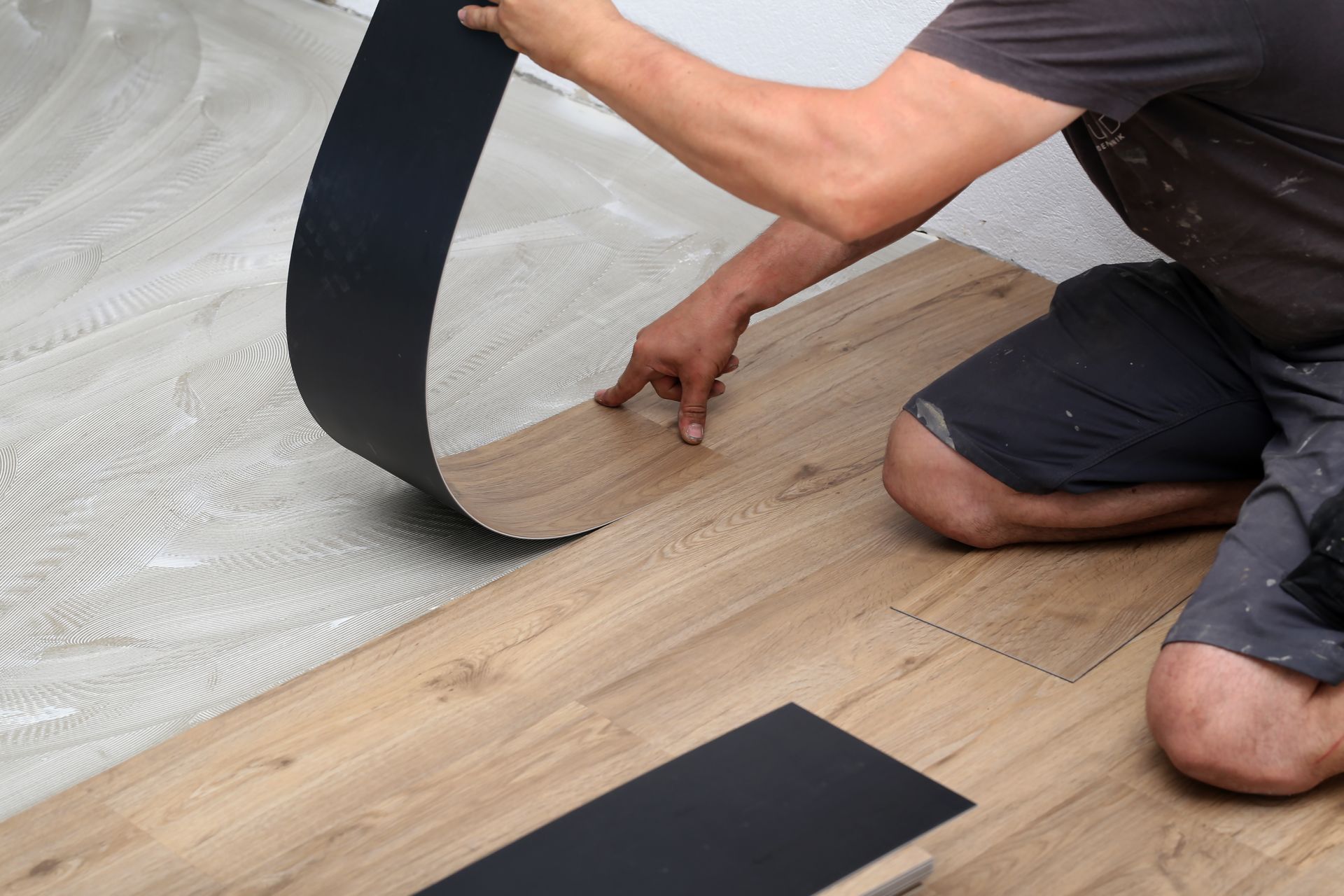 Person installing vinyl flooring plank, lifting sheet back to align wood-look floor. Person installing vinyl flooring plank, lifting sheet back to align wood-look floor.