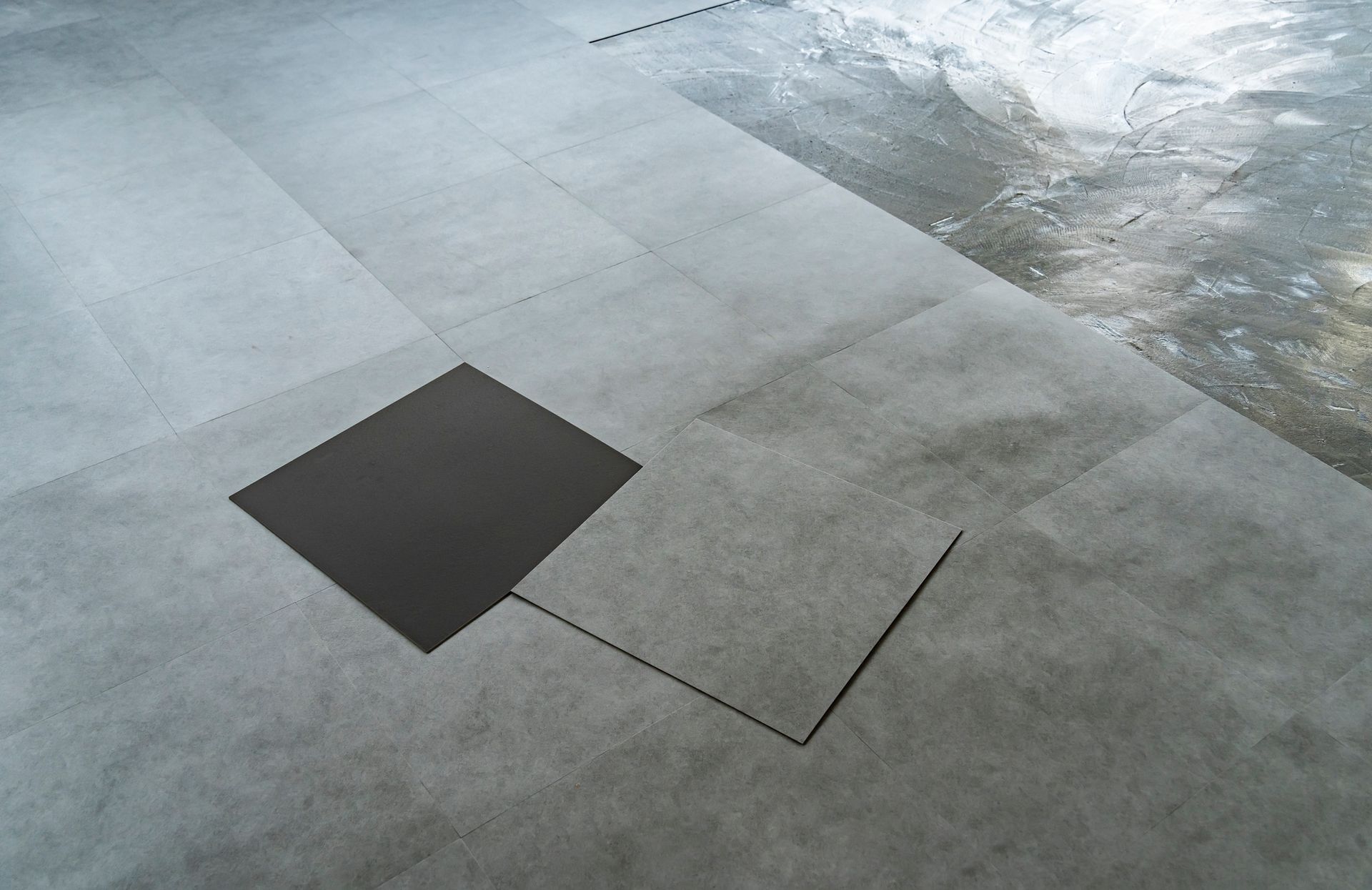 Gray tiled flooring with a dark square tile partially covering an adjacent tile, interior setting. Gray tiled flooring with a dark square tile partially covering an adjacent tile, interior setting.