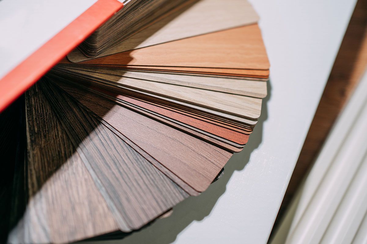 Color swatch fan, primarily wood tones, fanned out on white surface, with partial view of a paint roller.