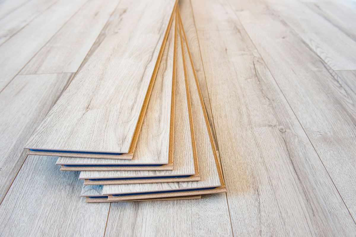 Stack of light-colored wood flooring planks, lying on top of more installed planks.