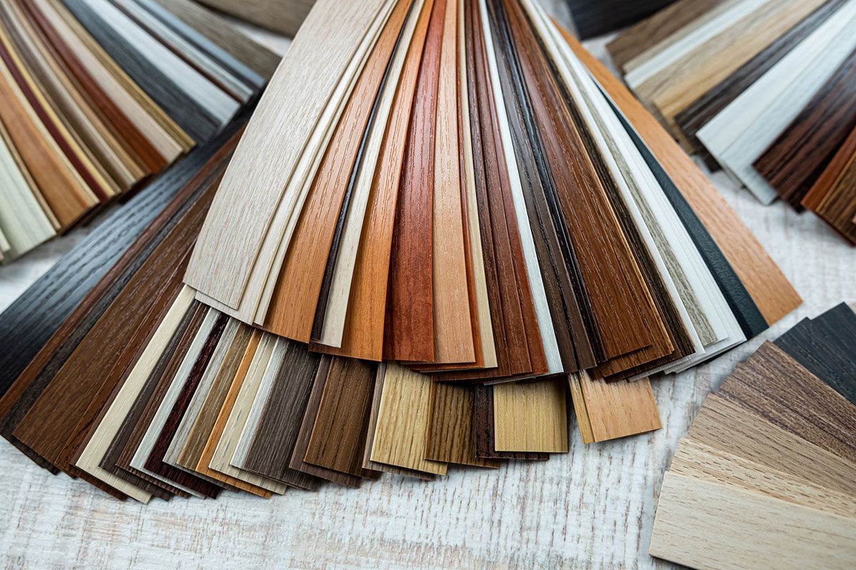 Wooden flooring samples in various shades, fanned out on a white wooden surface.