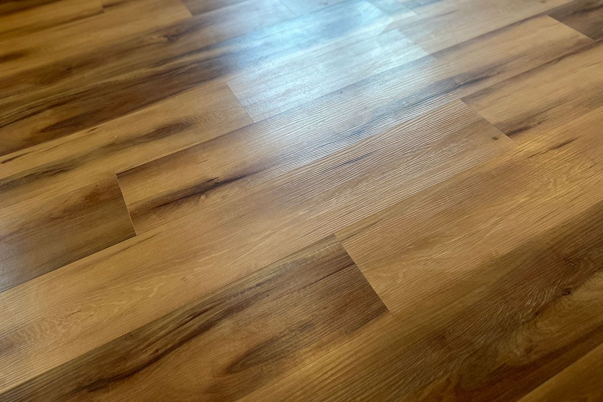 Close-up of a light-brown wood-look floor with a textured surface. Light reflects off the planks.