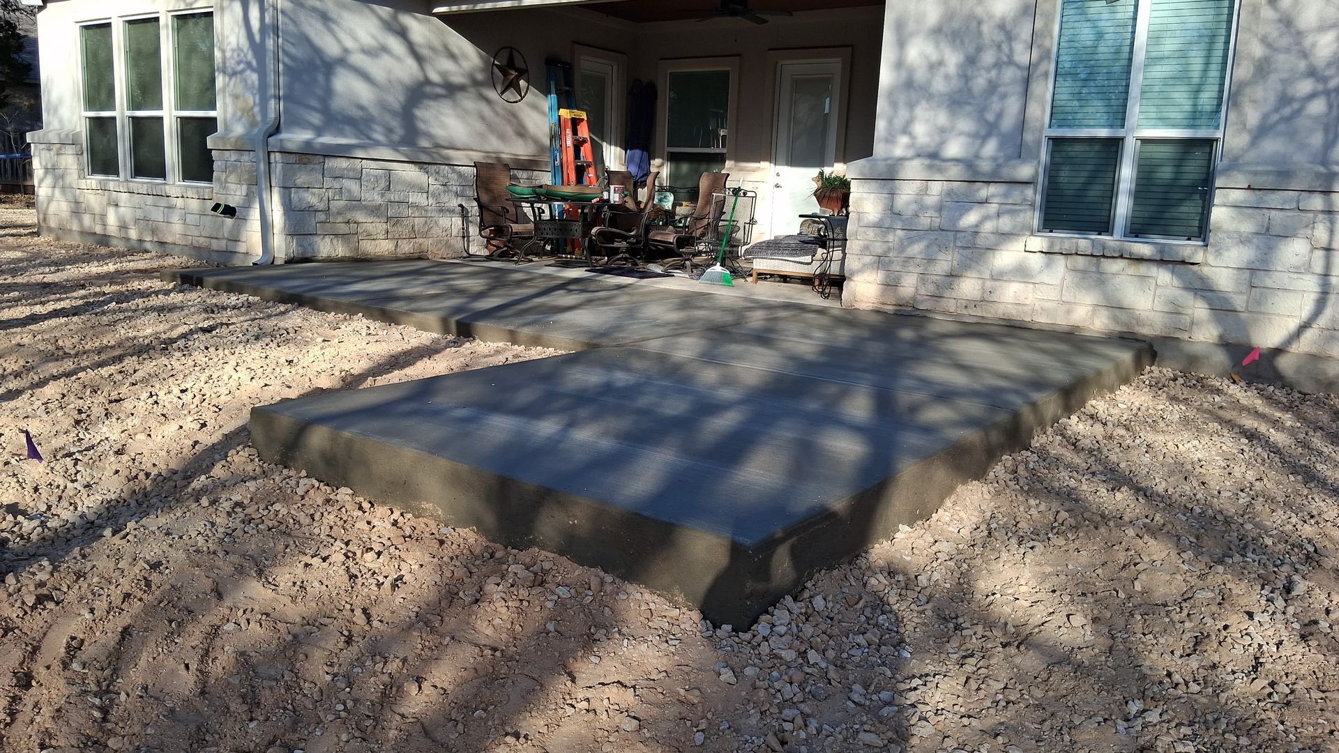 Concrete patio under construction, surrounded by gravel, next to a white house.