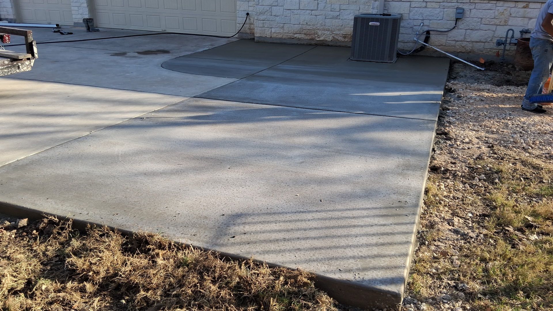 Freshly poured concrete patio extending from a building with a person working in the background.