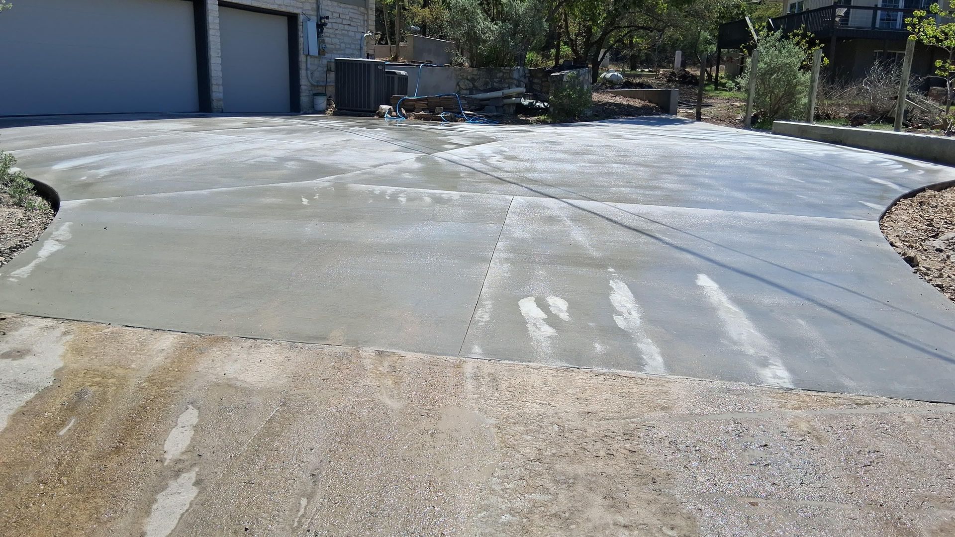 Freshly poured concrete driveway section transitioning into older exposed aggregate pavement in a residential setting.