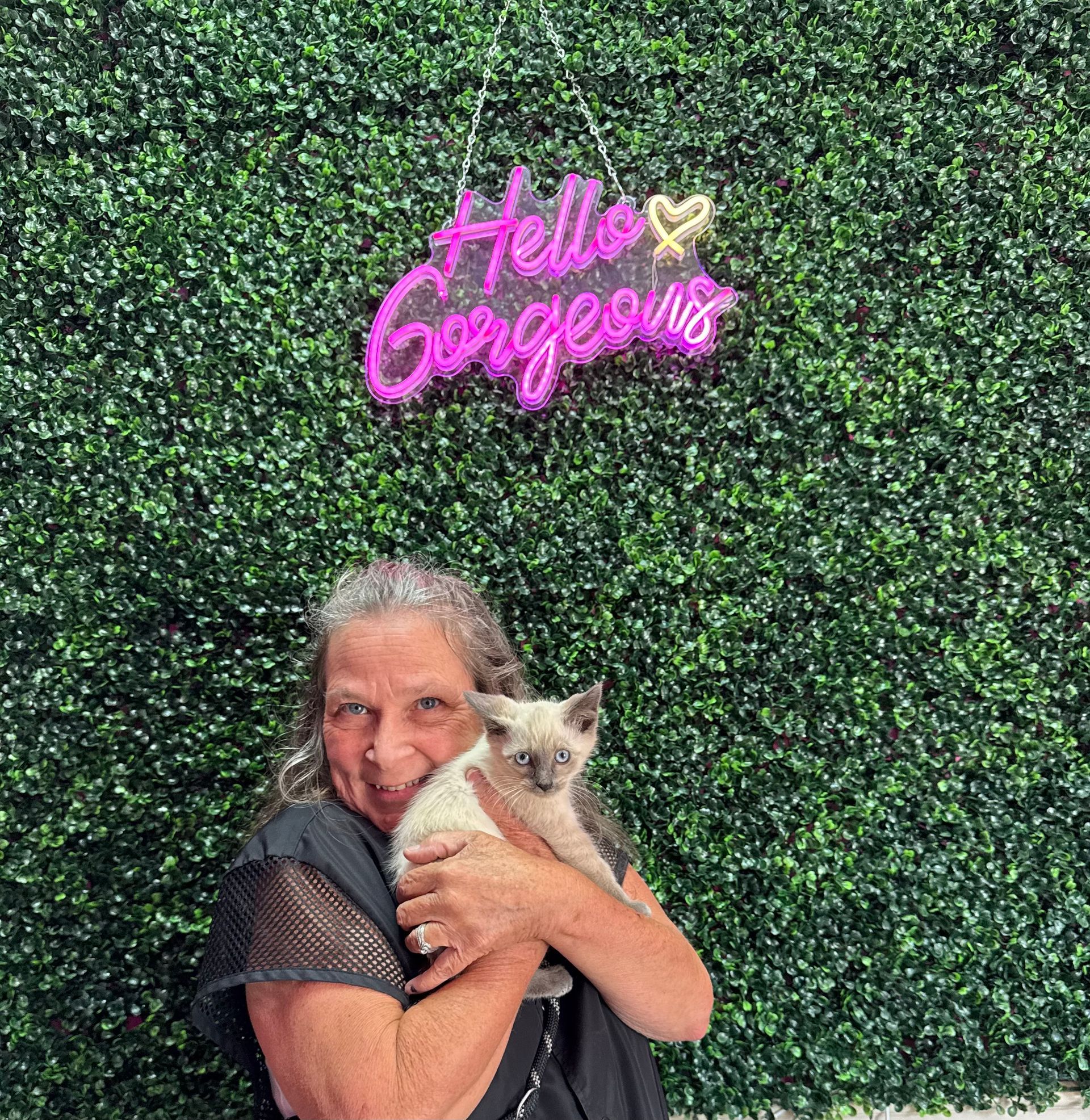 A woman is holding a cat in front of a green wall.