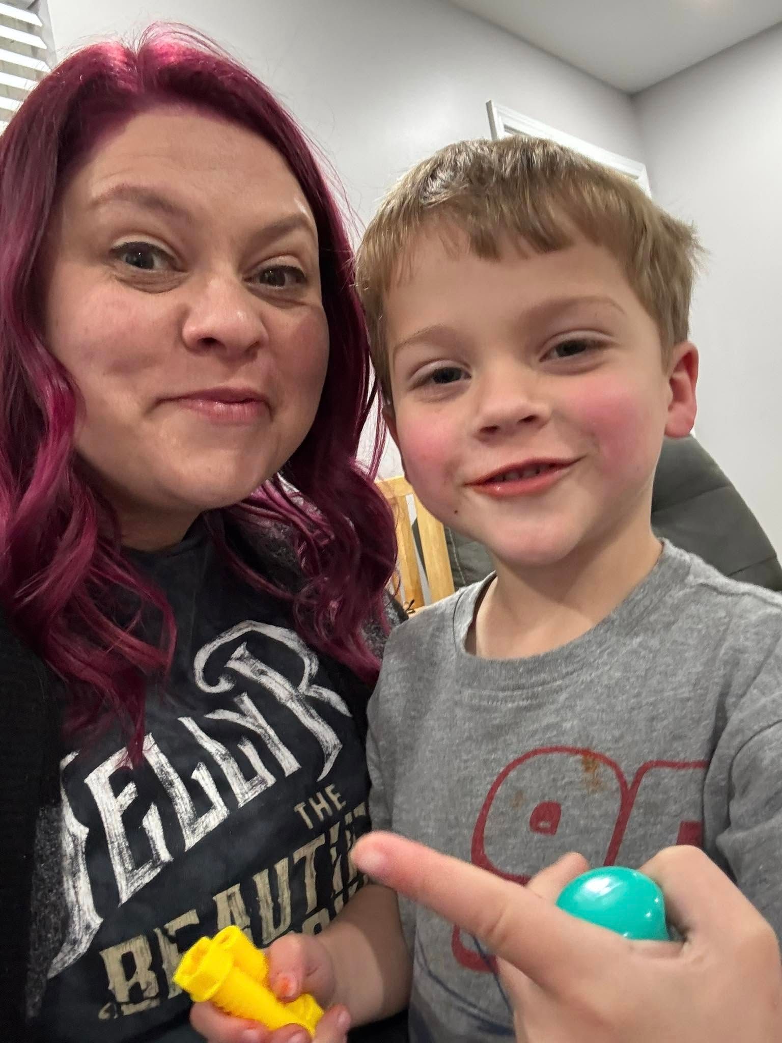 A woman and a boy are posing for a picture and the boy is pointing at something.