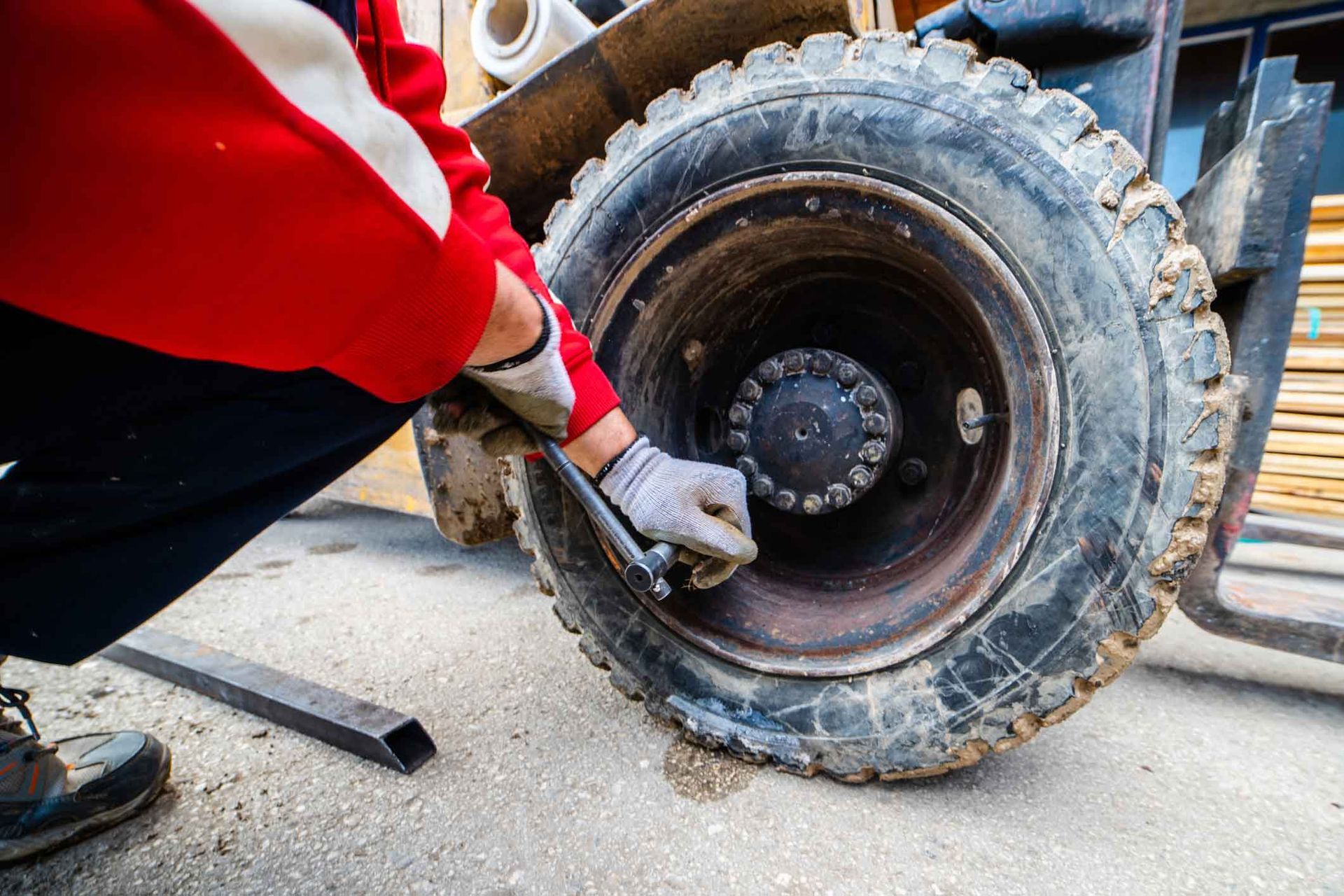 A man is changing a tire on a forklift with a wrench.