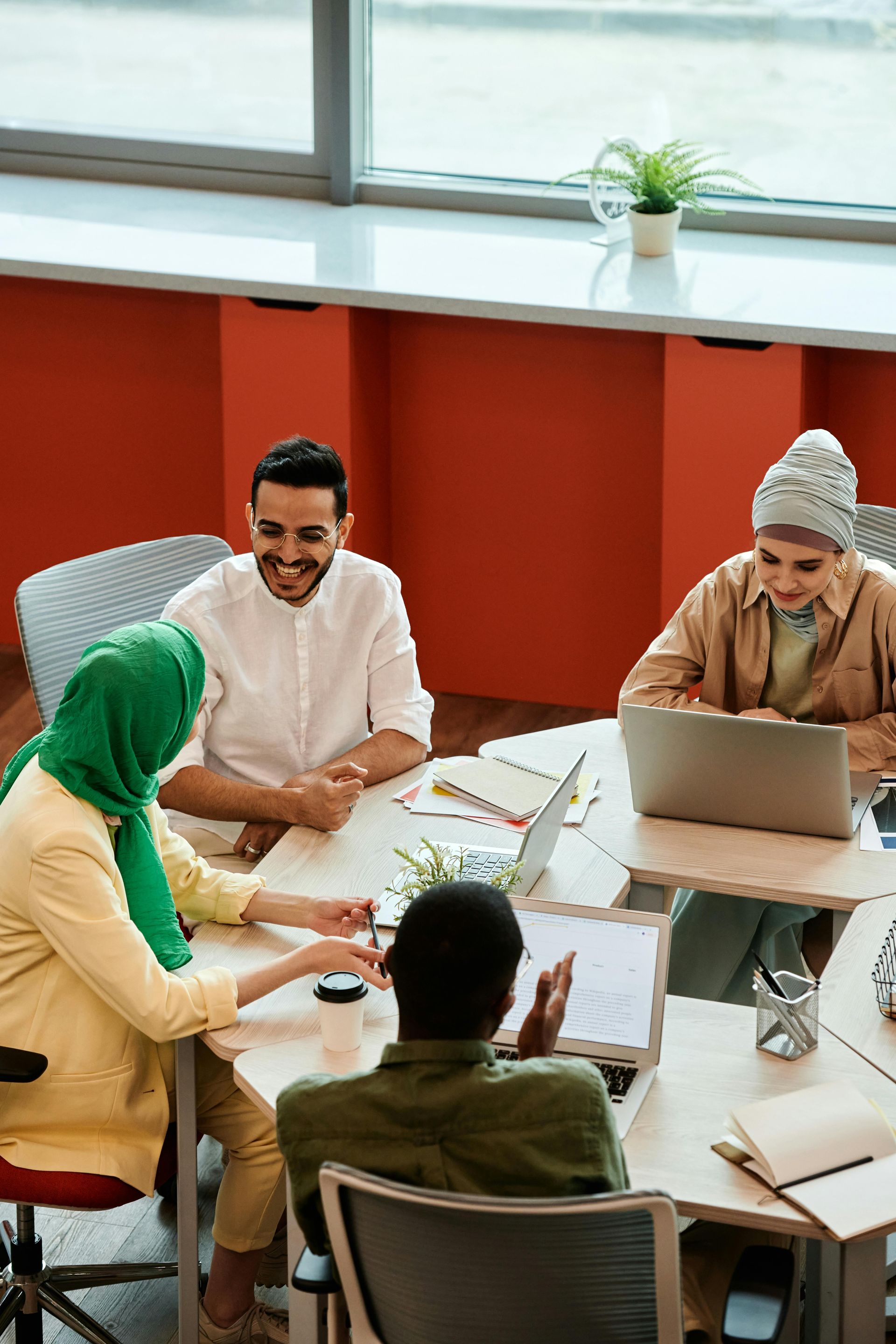 Group of people collaborating around a table. A person is working on a laptop while others are talking.