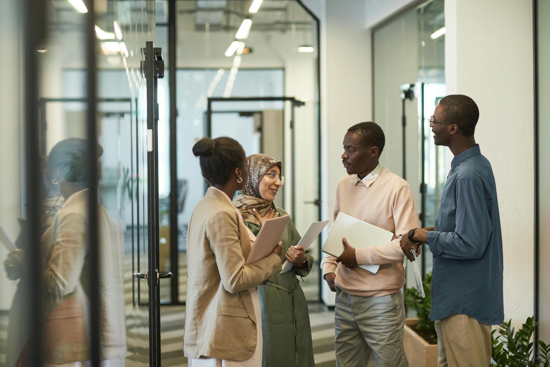 Four people in a modern office hallway, conversing and holding documents.