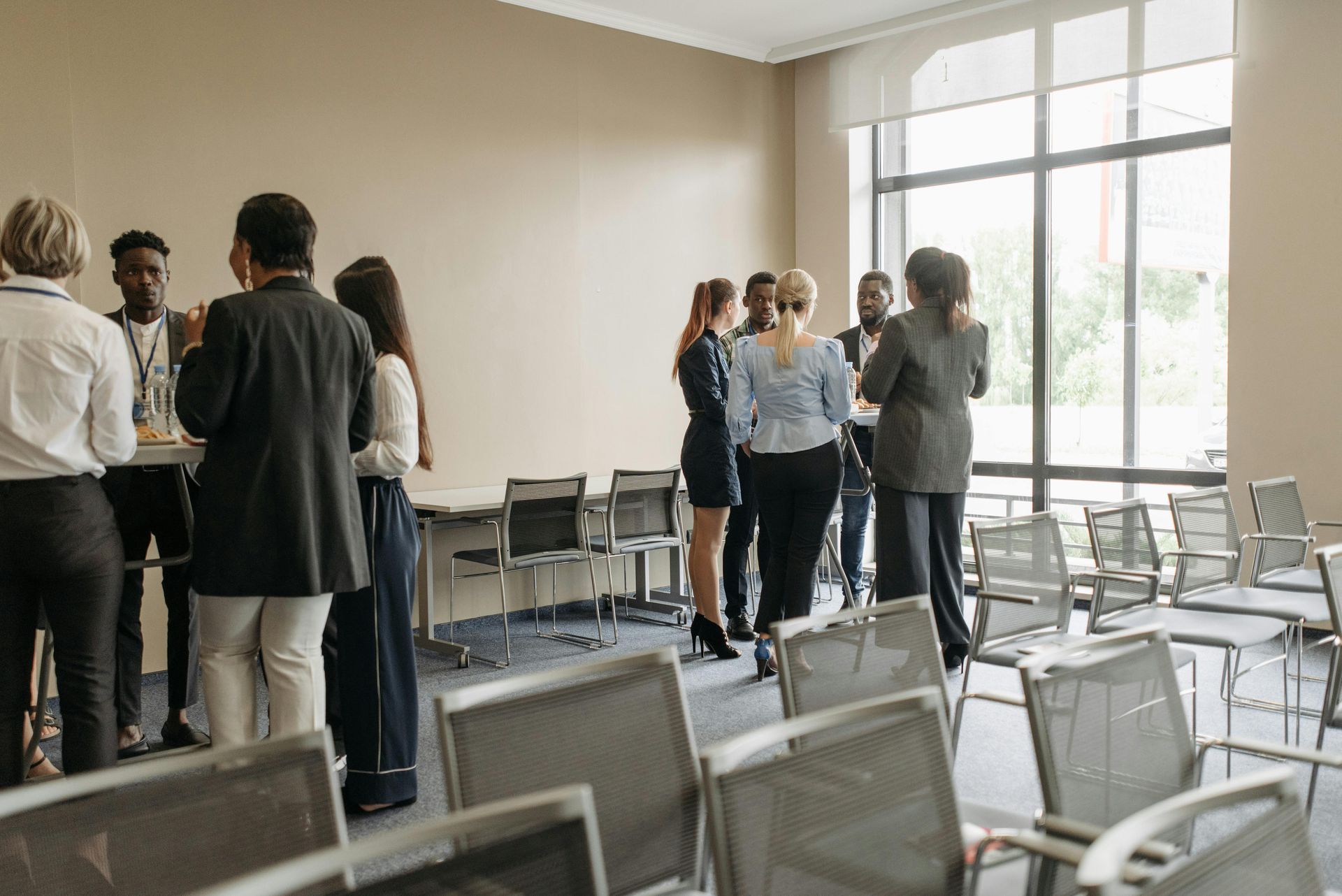 People in business attire networking in a conference room with chairs and a large window.