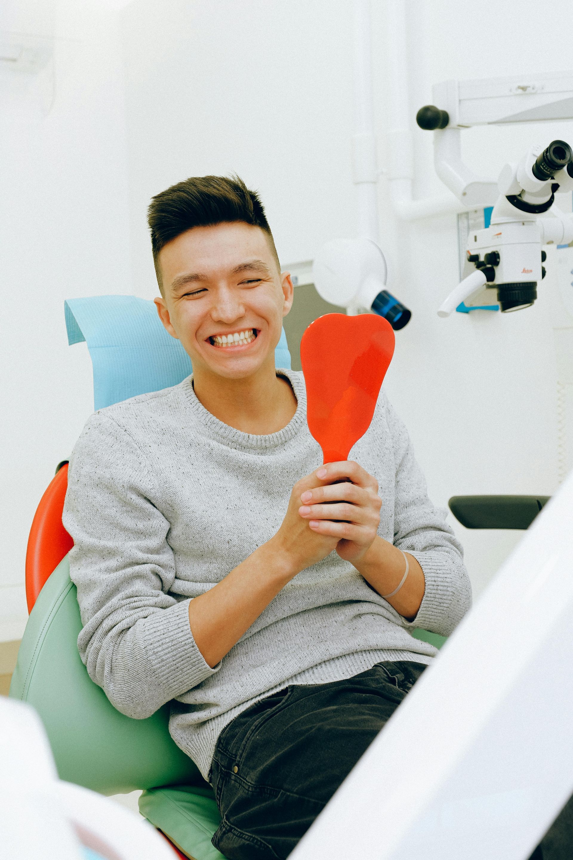 A man is sitting in a dental chair looking at his teeth in a mirror.