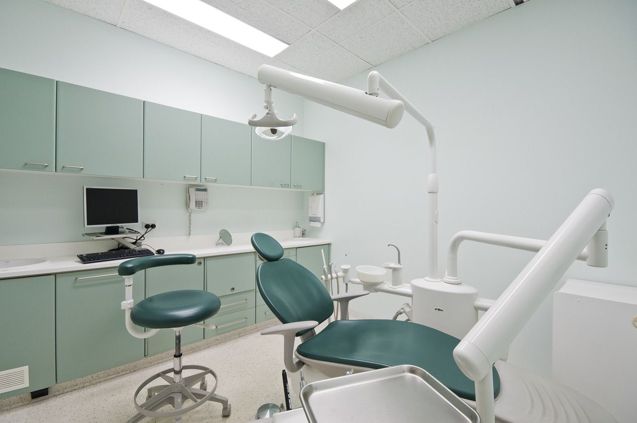 An empty dental office with a green chair and a computer