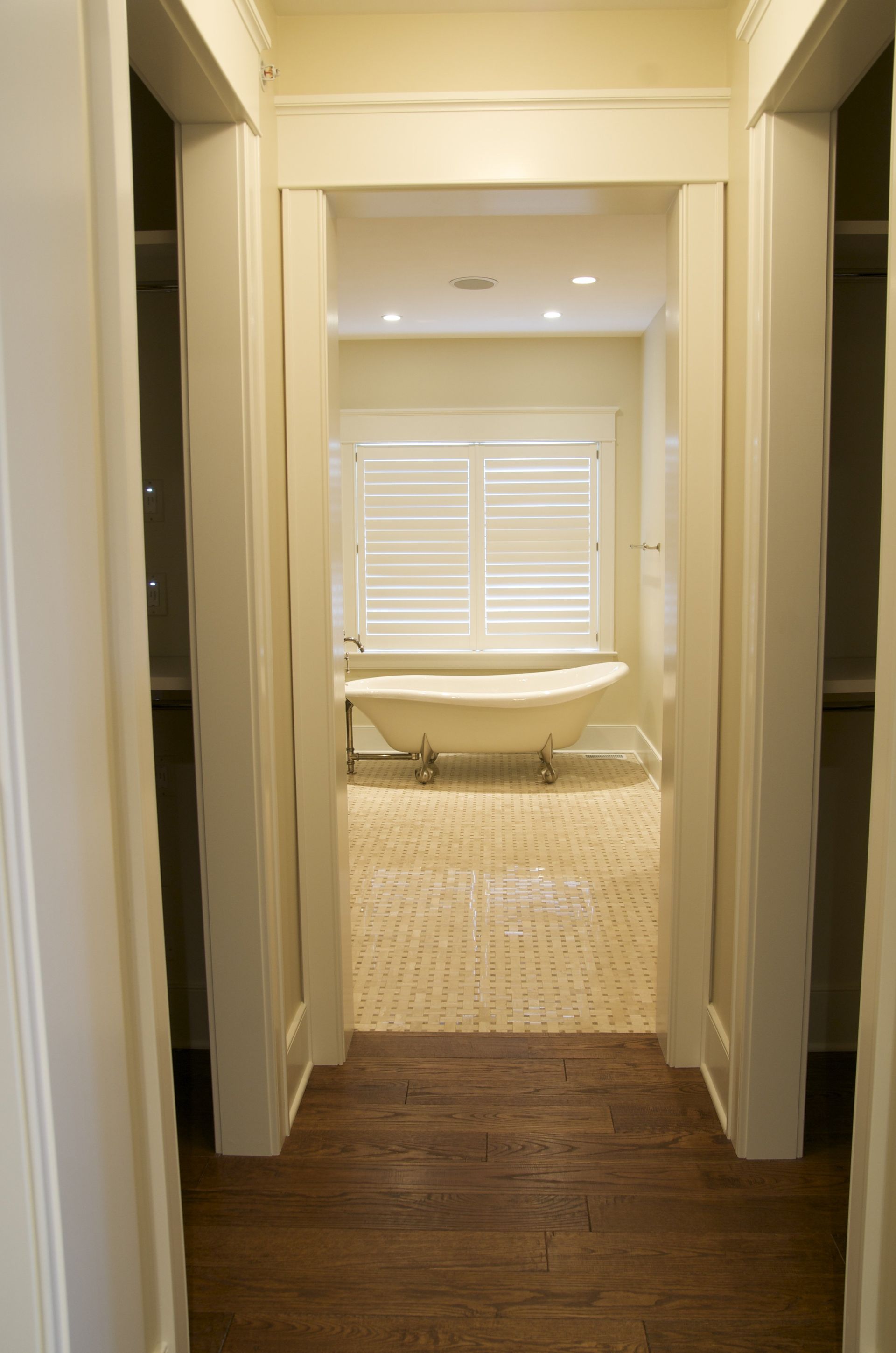 A hallway leading to a bathroom with a tub and a window.