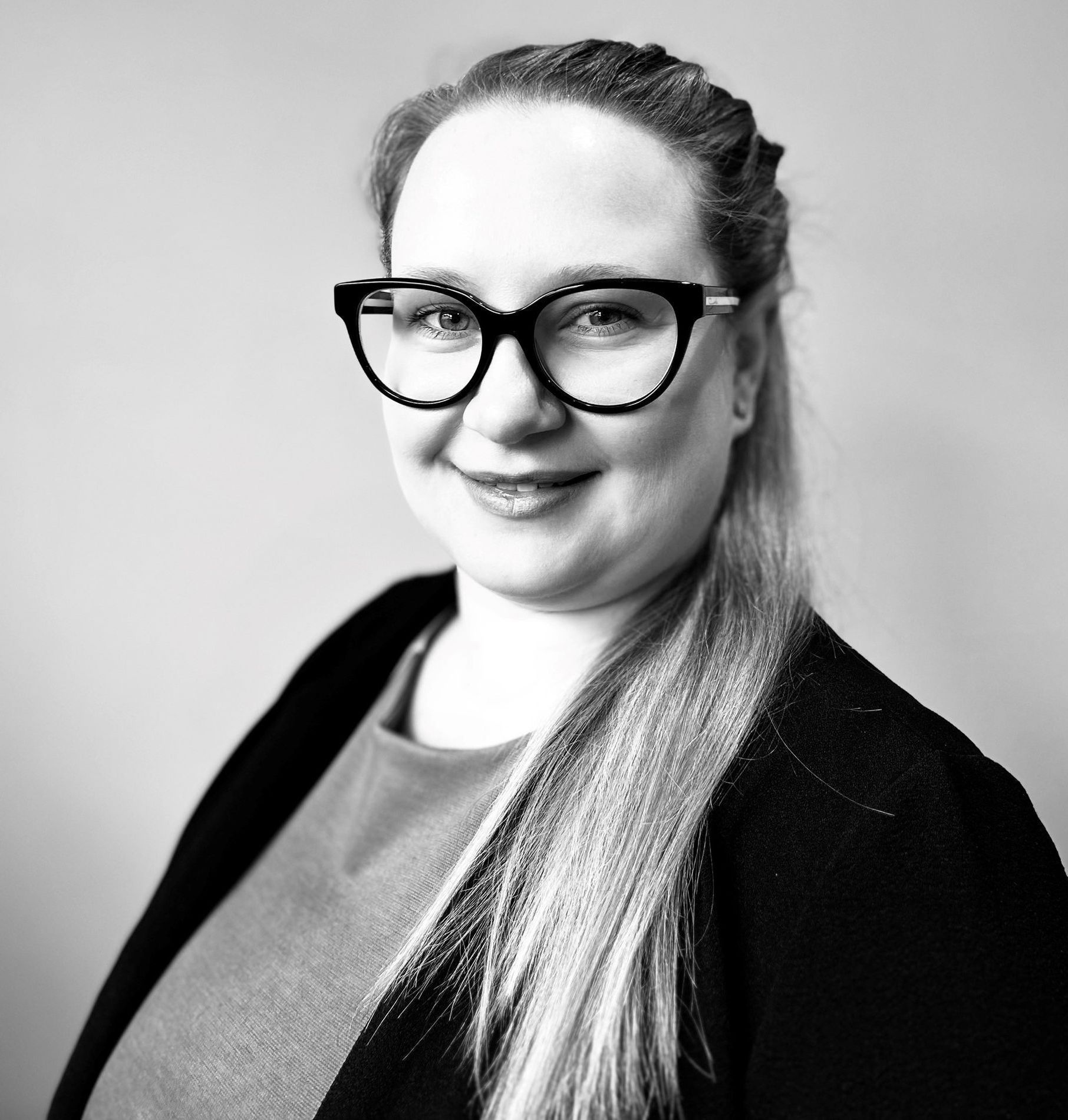 A woman wearing glasses and a black jacket is smiling in a black and white photo.