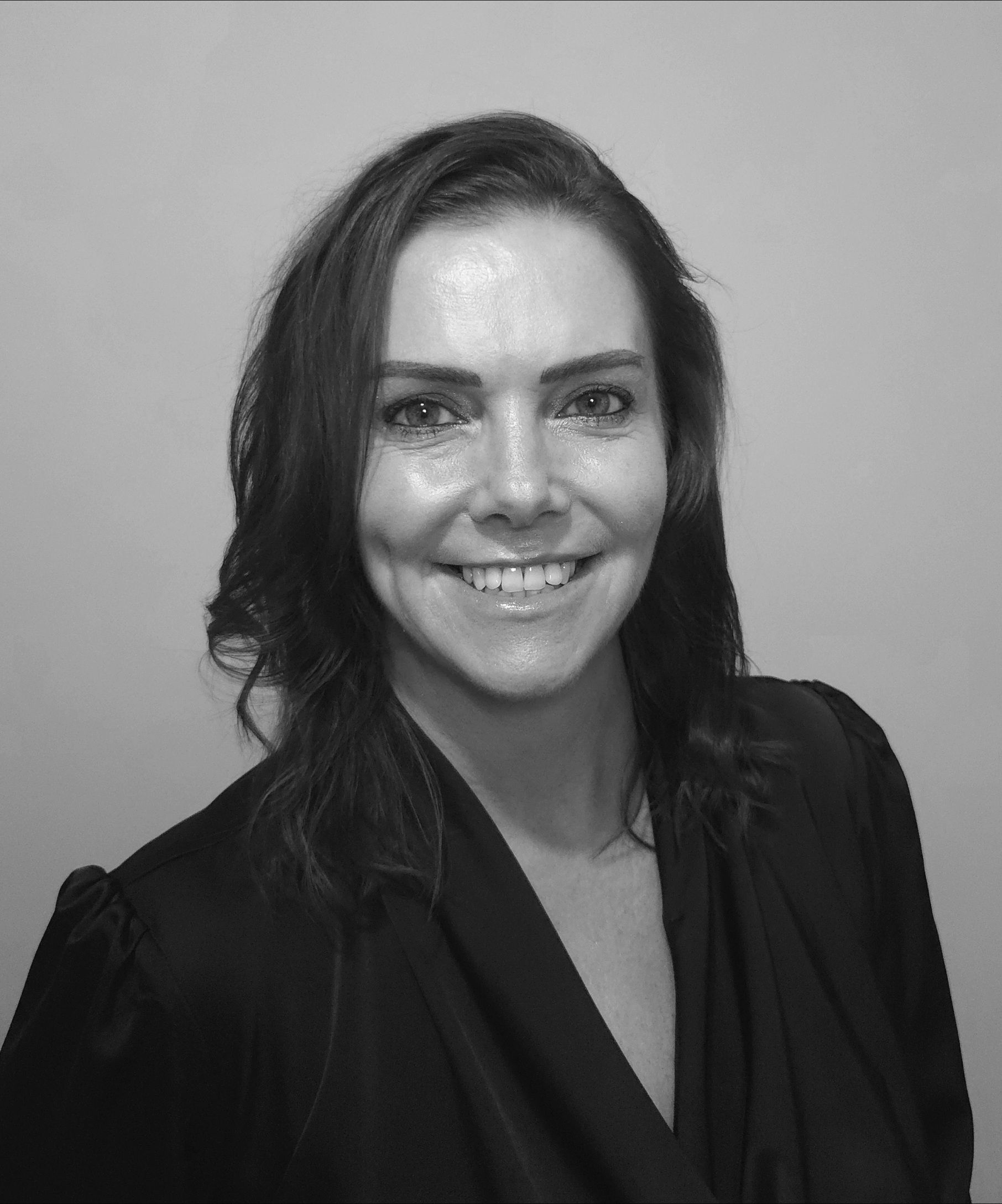 A woman in a black jacket is smiling in a black and white photo.
