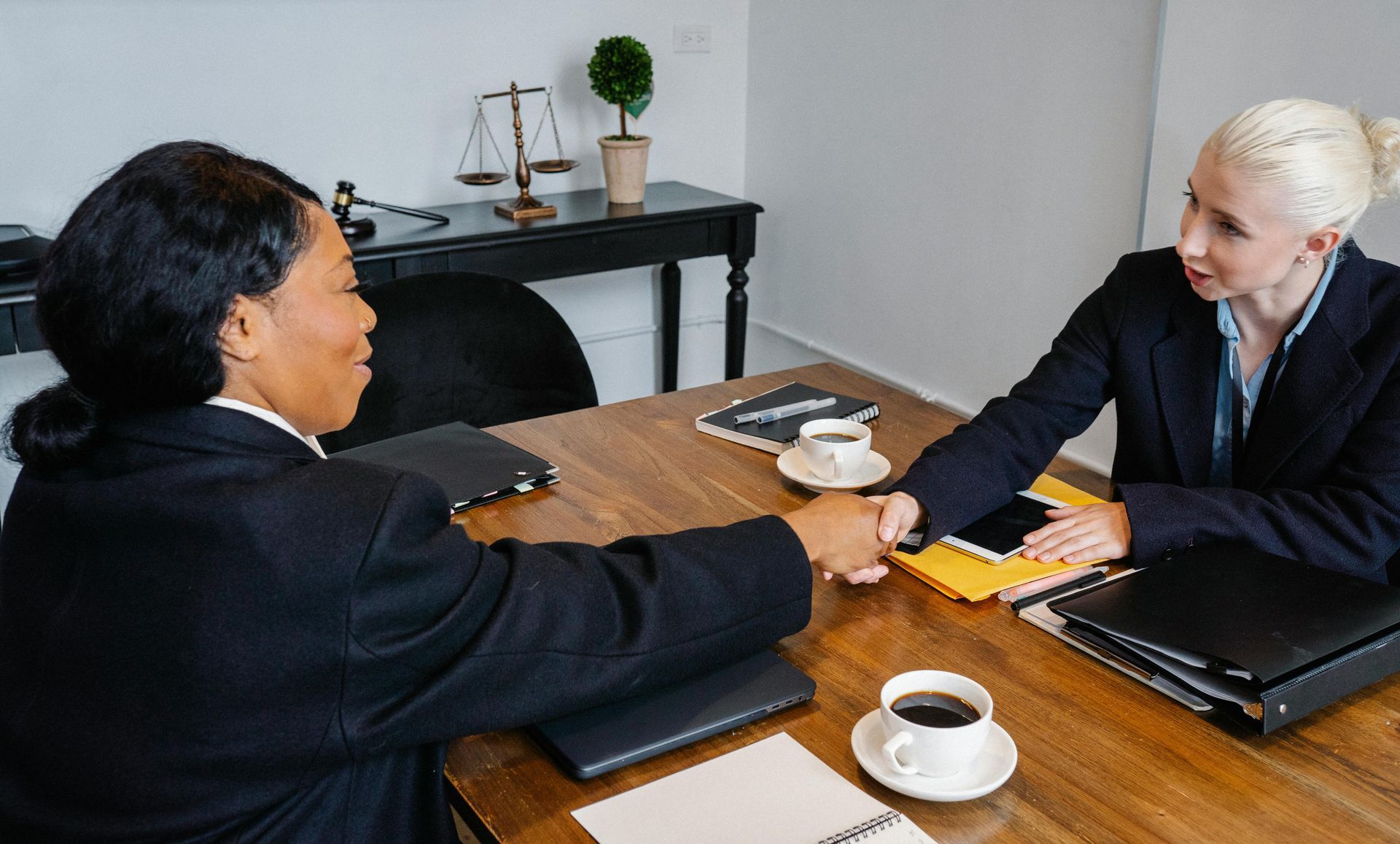 Two women are shaking hands while sitting at a table.