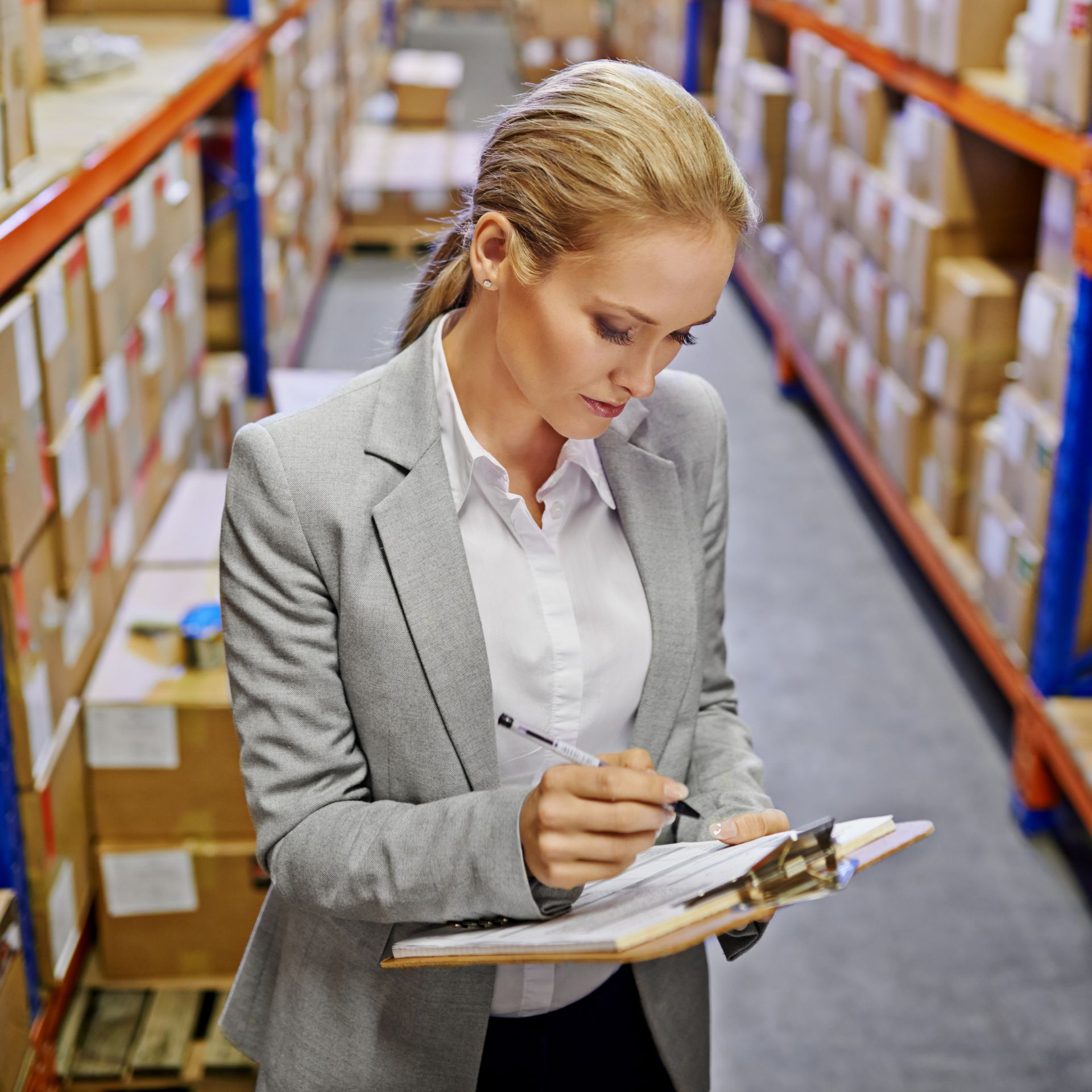 A woman is writing on a clipboard in a warehouse