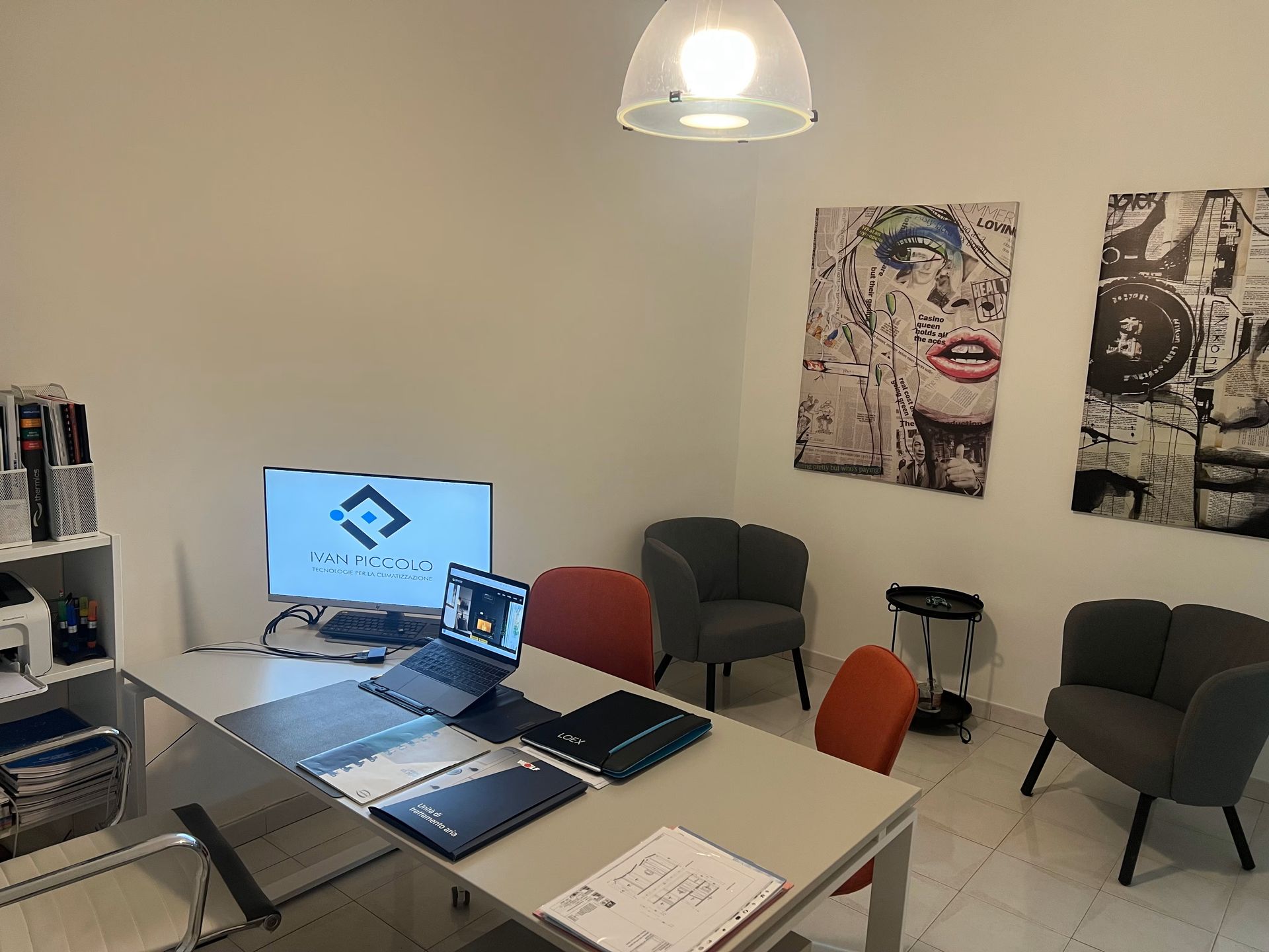 Ufficio con scrivania, computer, quadri e sedie. Pareti bianche, luce intensa e stampante a vista.