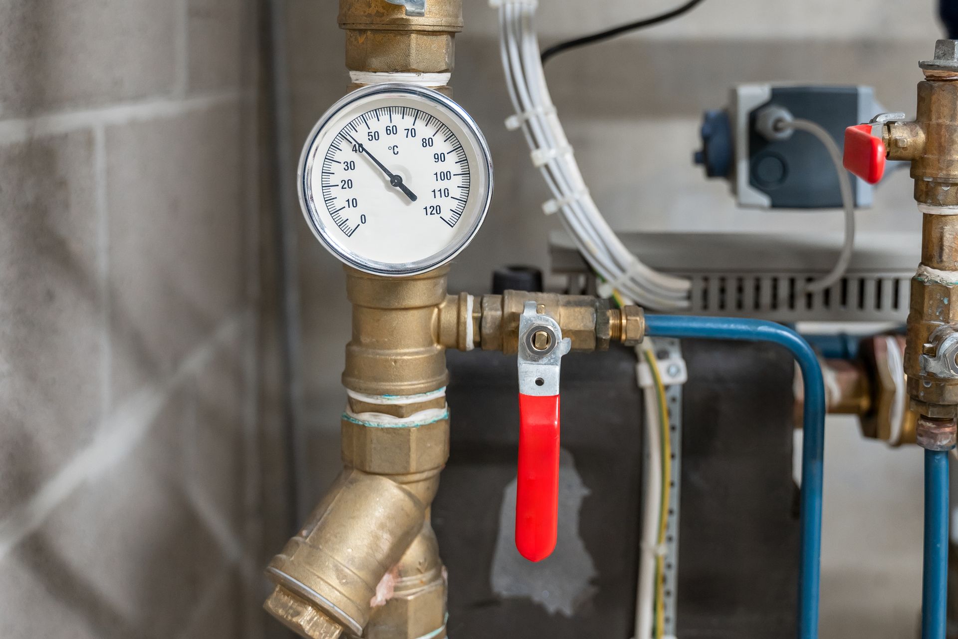 Manometro su tubi di ottone, con valvola rossa, accanto a un impianto di riscaldamento.
