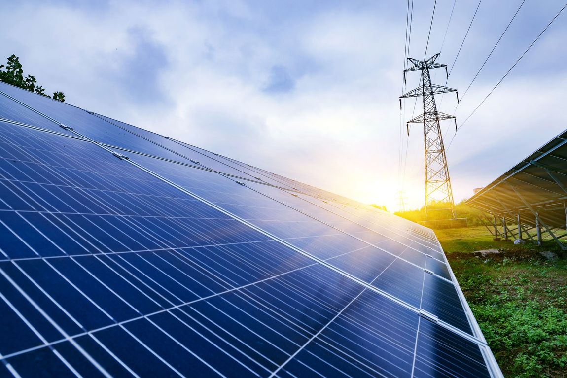 Pannelli solari con linee elettriche, luce solare intensa e cielo nuvoloso in un ambiente rurale.