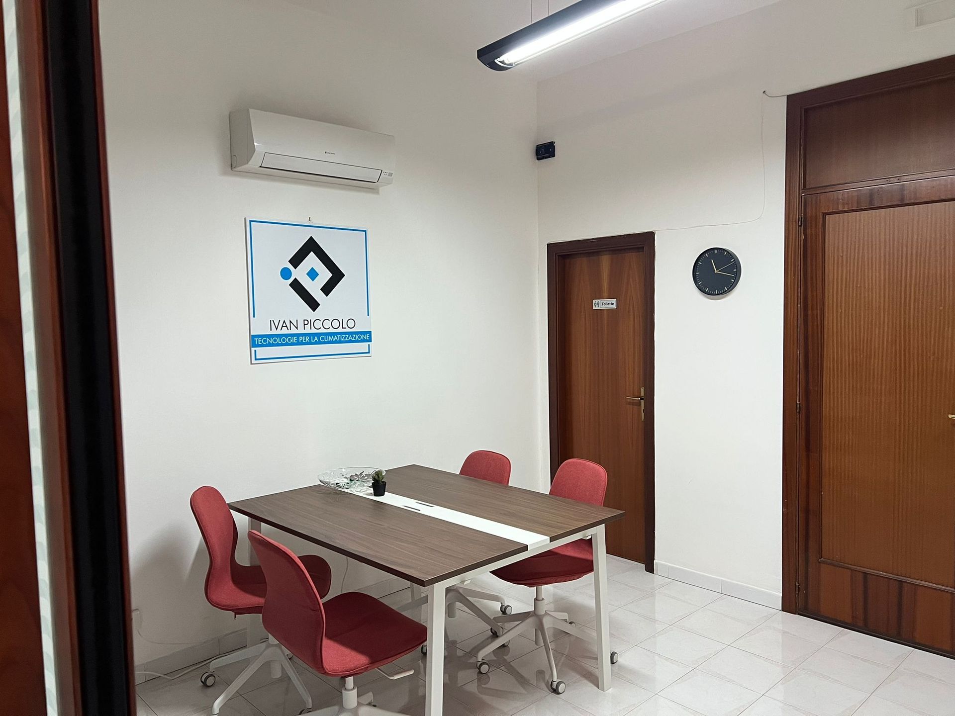 Ufficio interno con tavolo da pranzo, sedie rosse, porte aperte verso gli spazi di lavoro e opere d'arte.