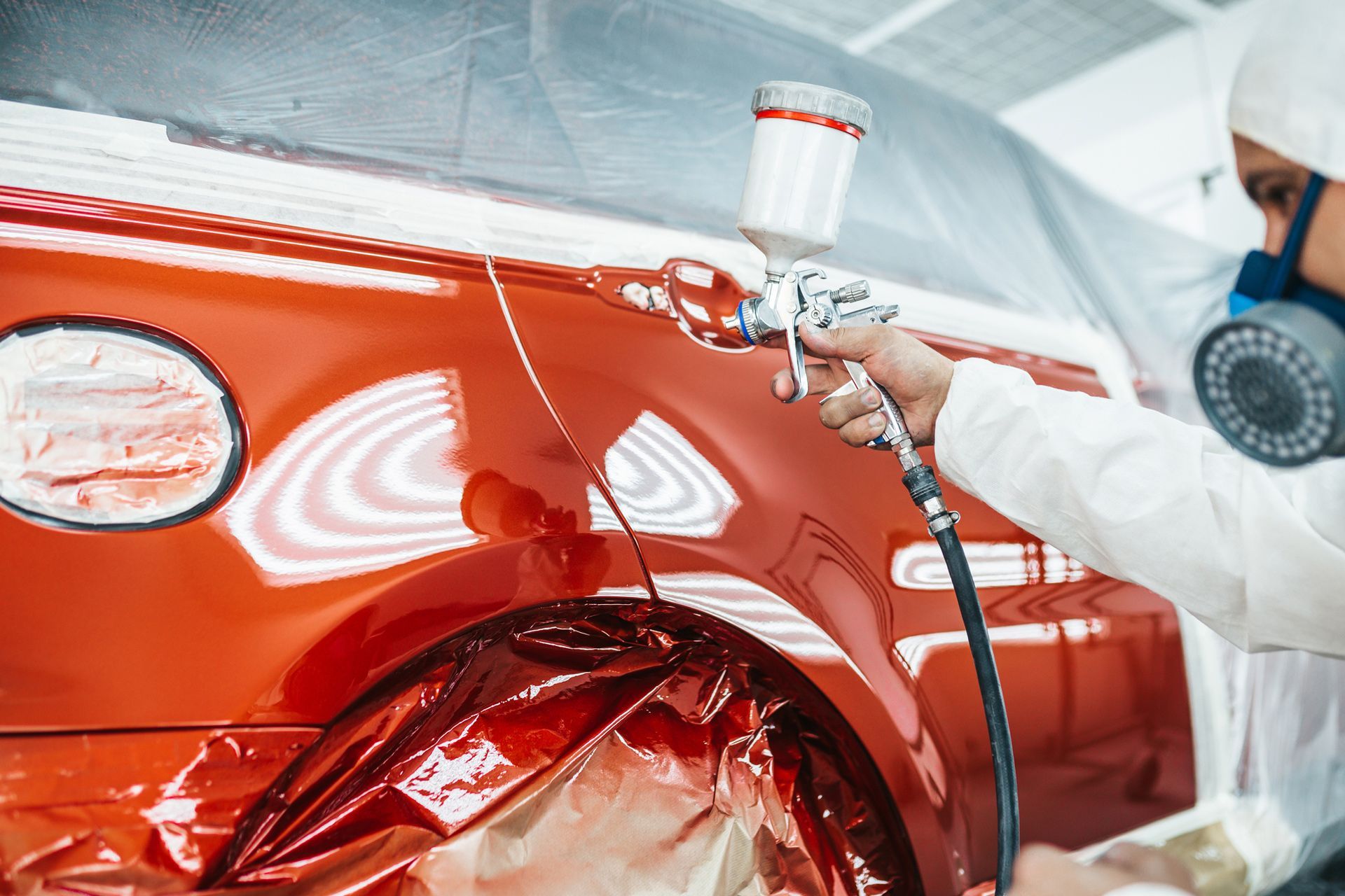 A man is spray painting a red car in a garage.