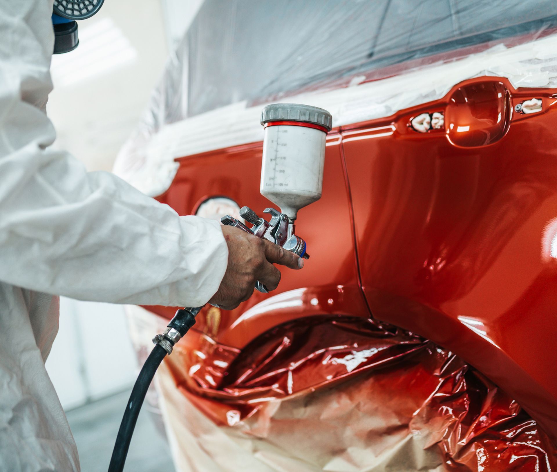 A man is spray painting a red car in a garage.