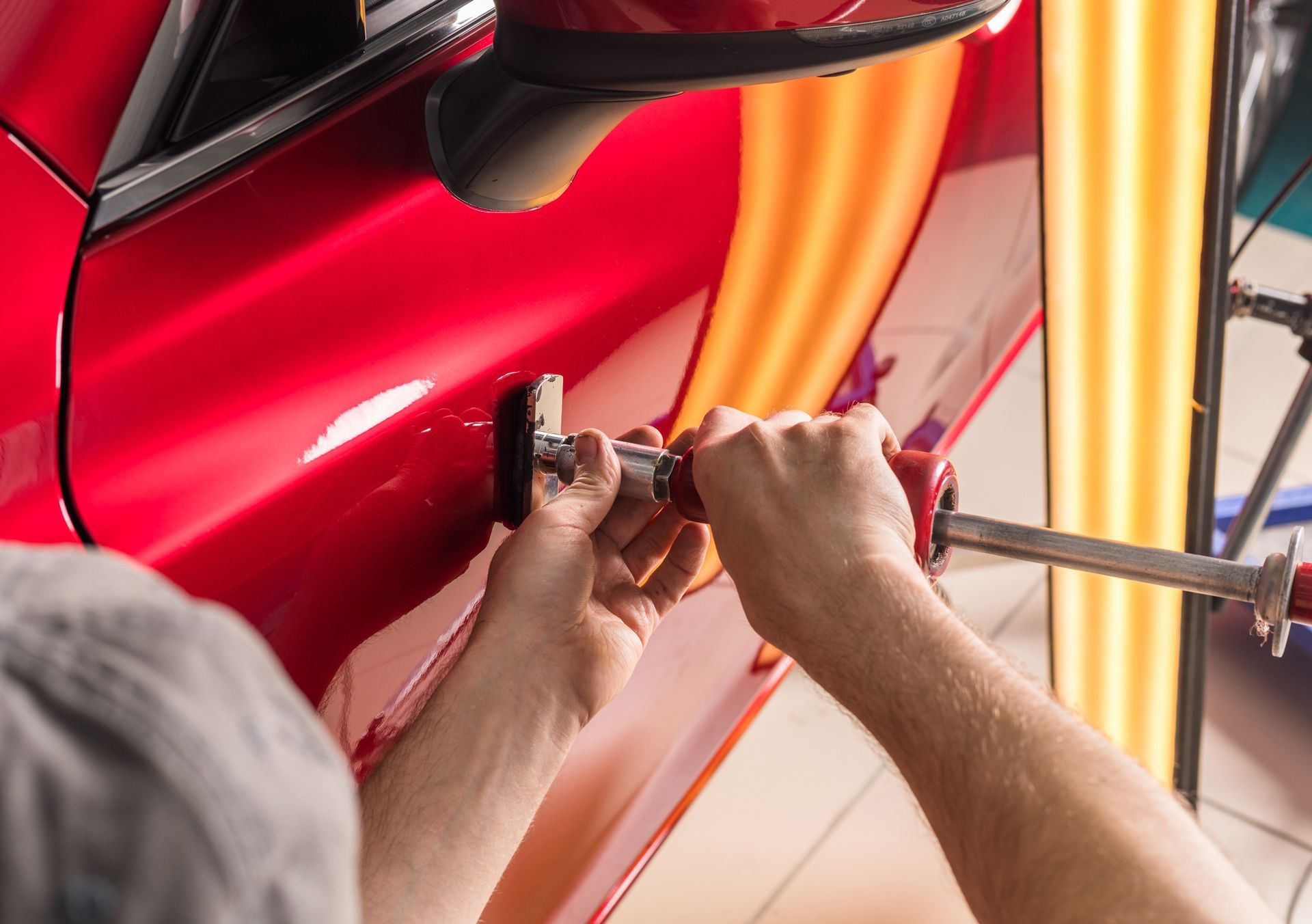 A man is working on a red car with a wrench.
