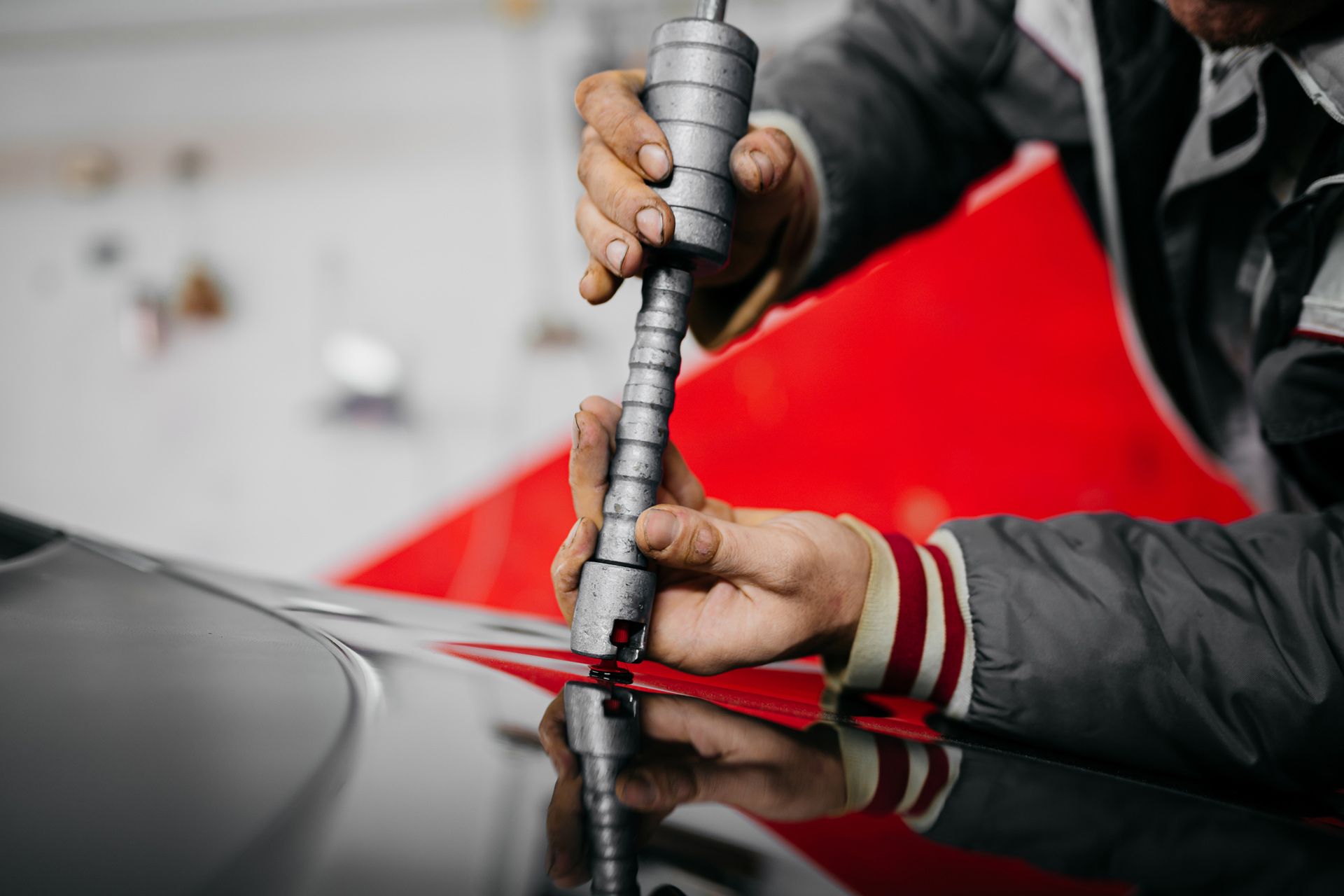 A man is working on the hood of a car with a tool.