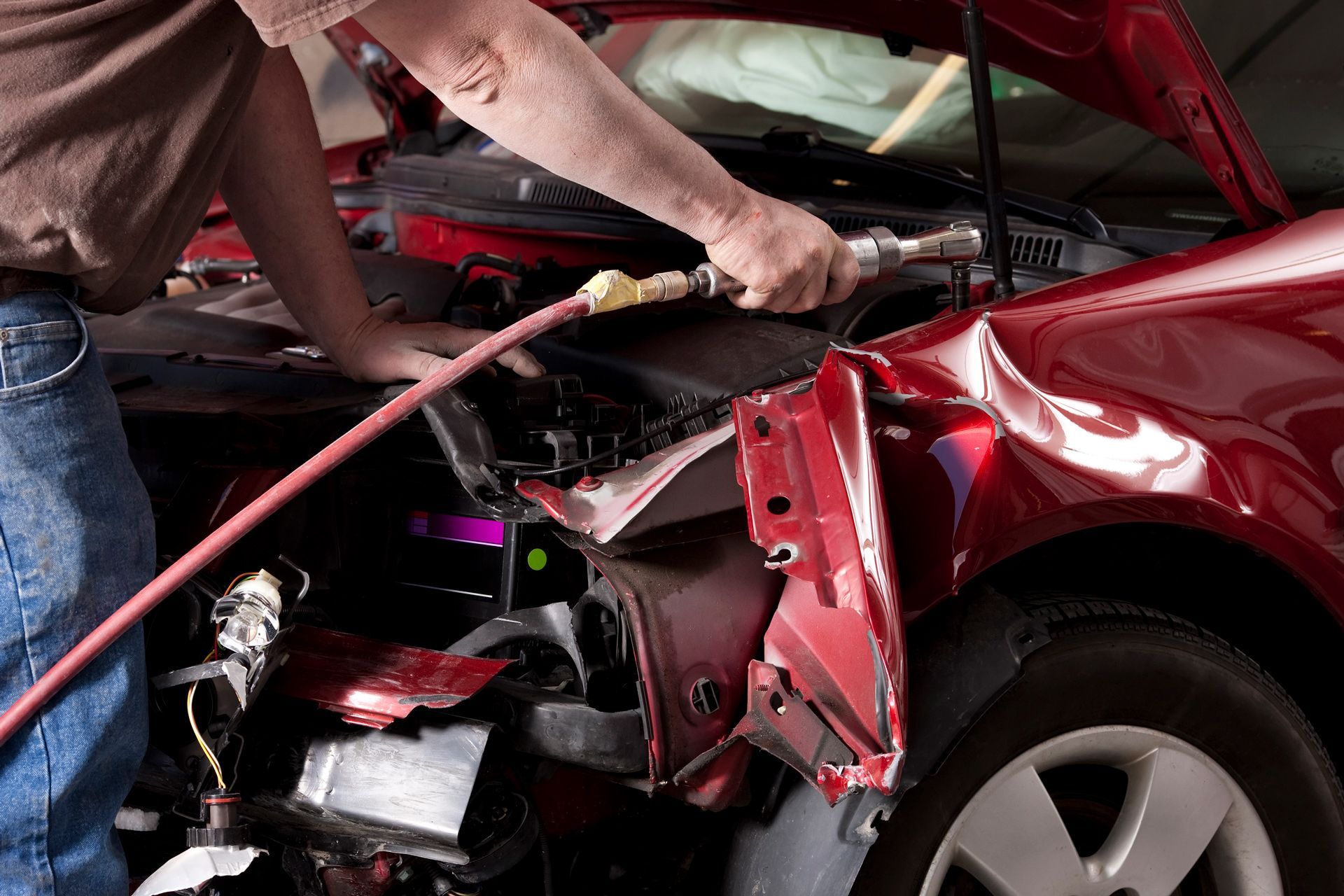 A man is working on a damaged red car with a hose.