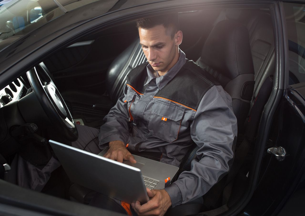 A man is sitting in the driver 's seat of a car using a laptop computer.