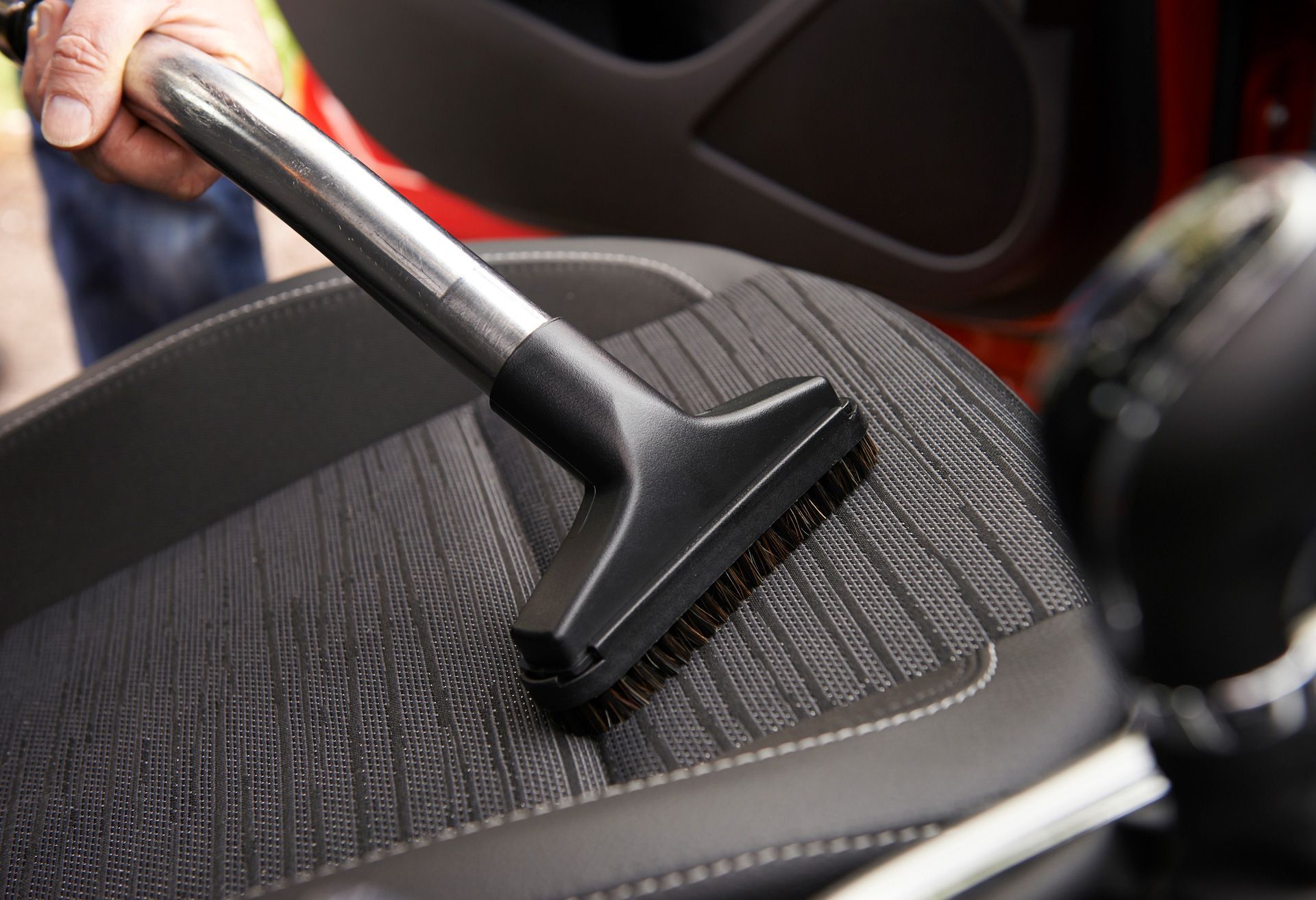 A person is cleaning a car seat with a vacuum cleaner