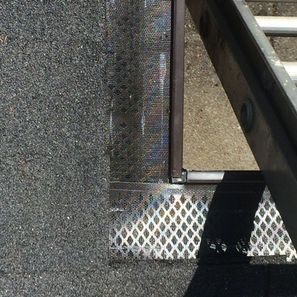 Black asphalt roof edge with metal gutter guard and brown metal trim; ladder leans against the side.