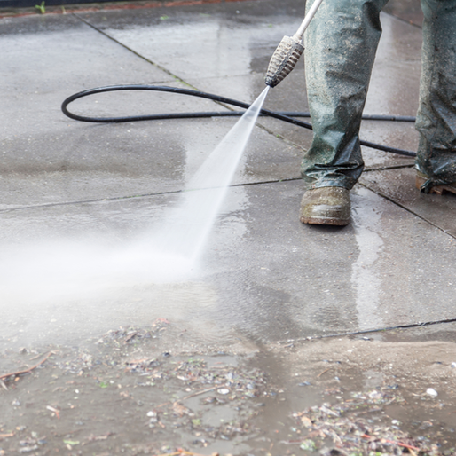 Person in work clothes power washing a concrete surface.